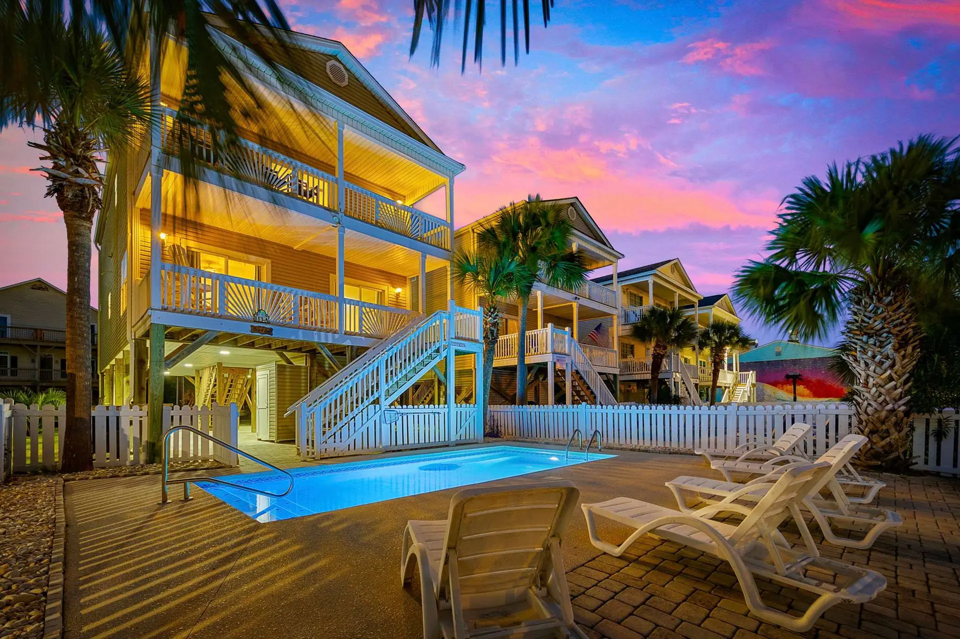 Oceanfront beach houses with a pool and lounge chairs under a sunset sky.