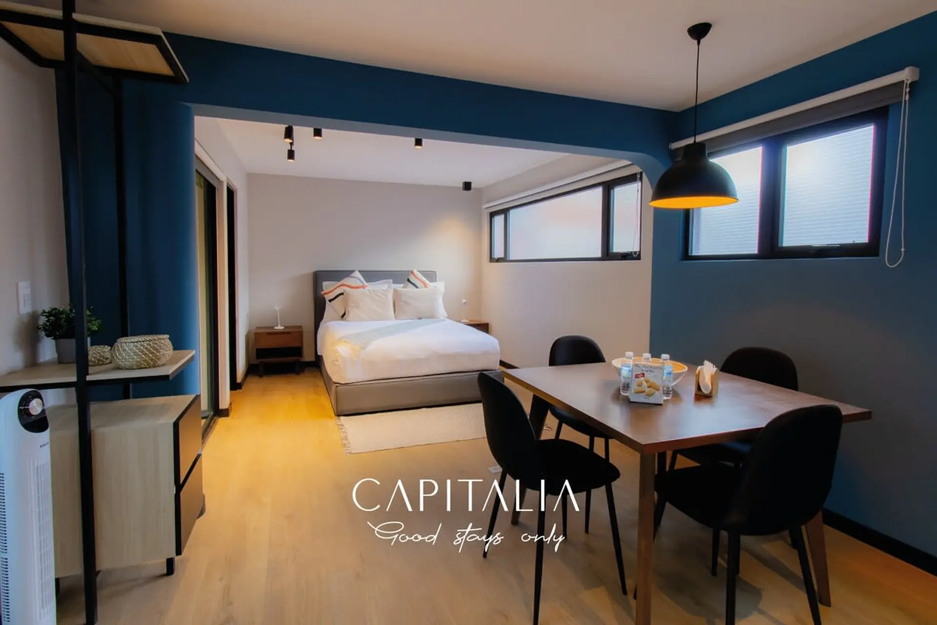 A modern hotel room with a bed, dining table, and blue walls.