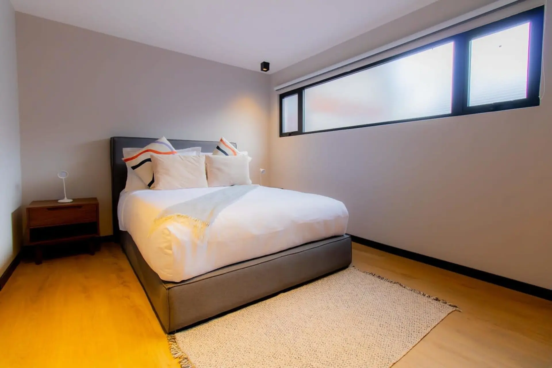A modern bedroom features a grey platform bed with white linens and decorative pillows, a wooden nig