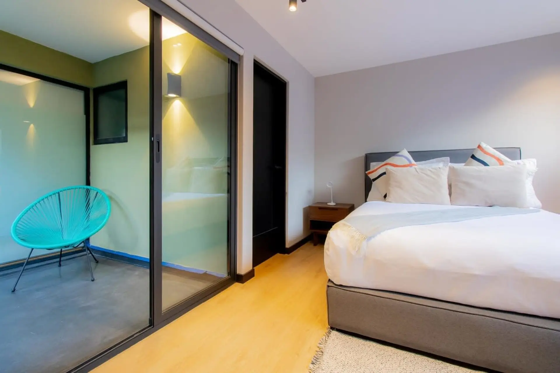 A modern bedroom with a teal chair on a balcony and a bed with decorative pillows.