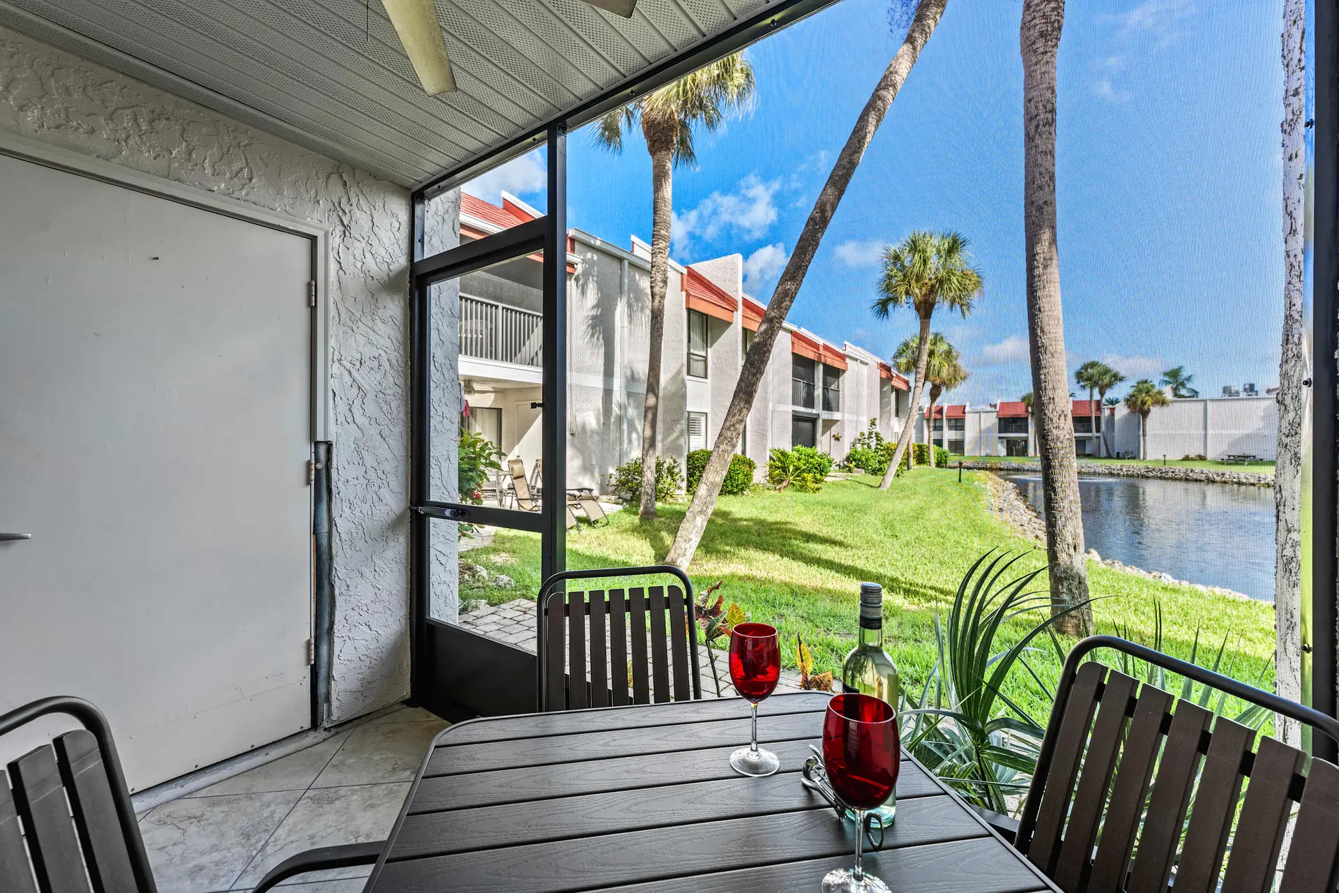 Screened patio with dining table, wine glasses, bottle, and chairs with view of building and water.