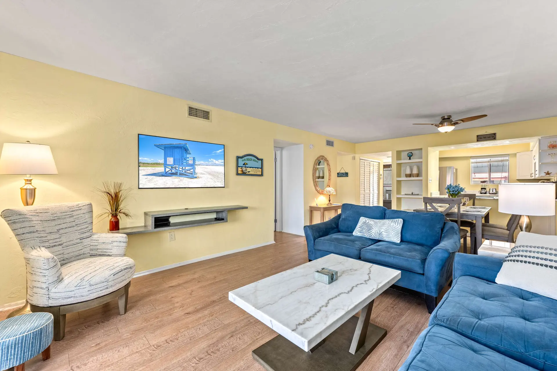 A living room with blue sofas, a marble coffee table, and a tv displaying a beach scene.