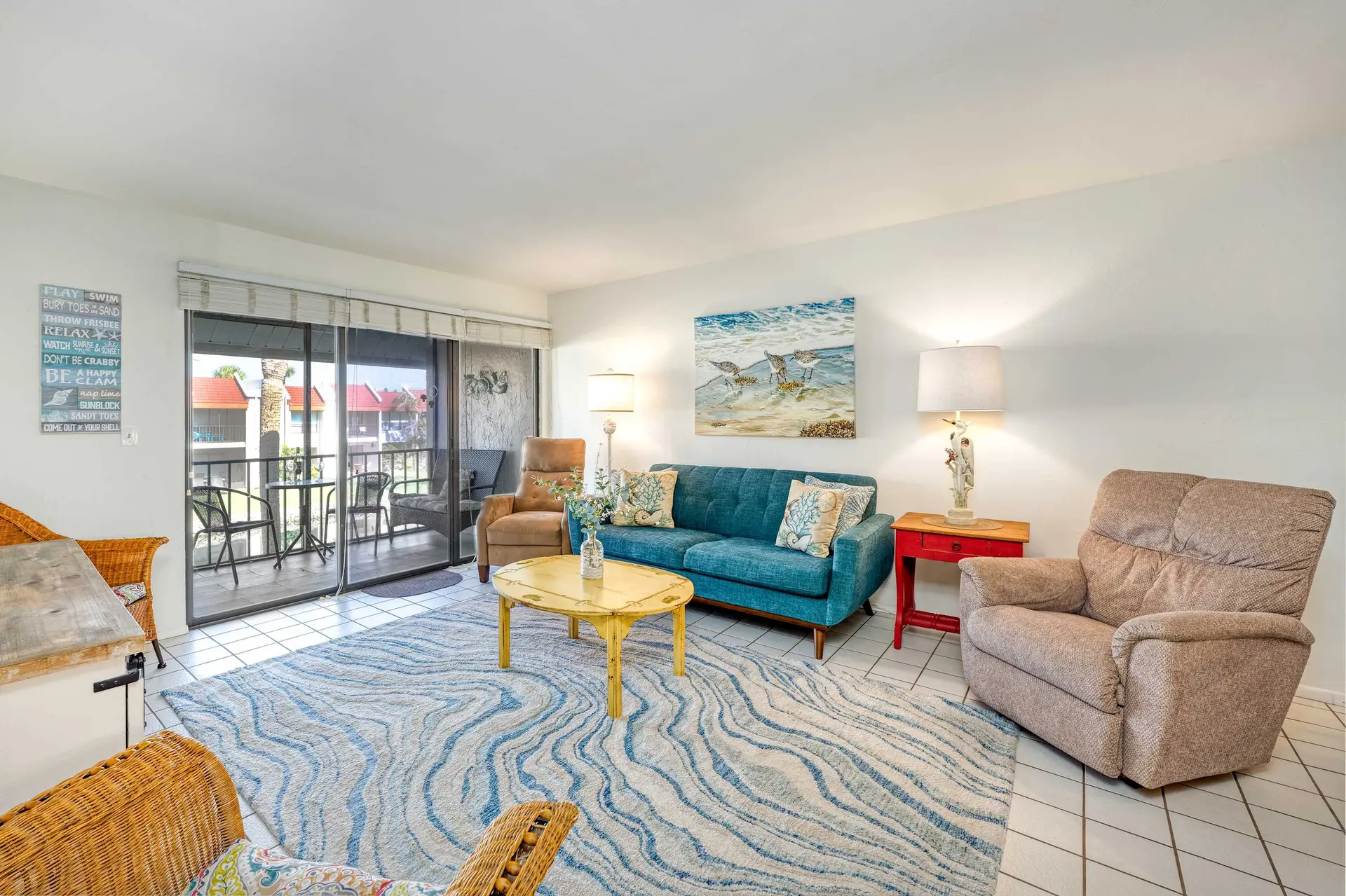 A living room with a blue sofa, chairs, and a balcony with ocean views.