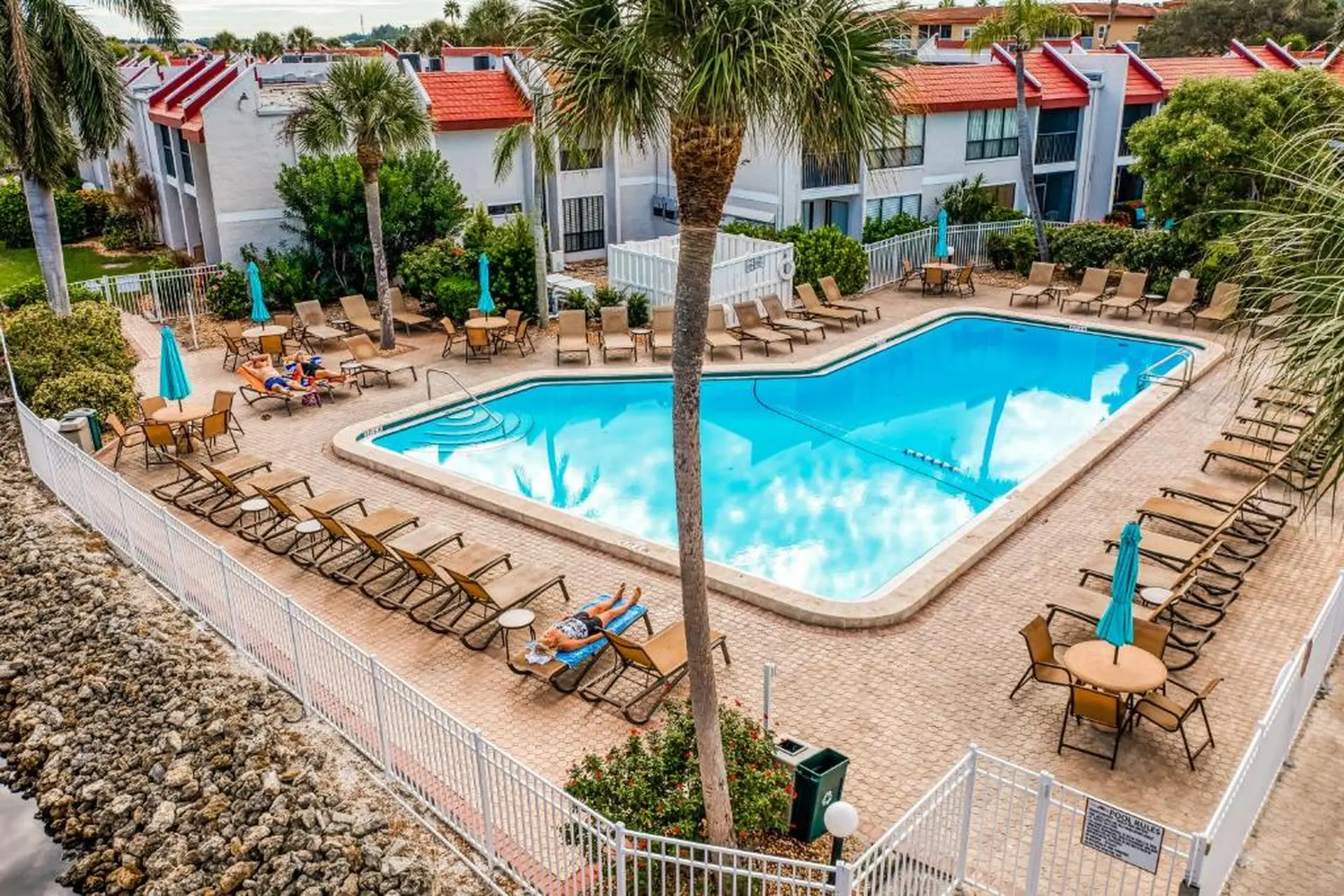 A serene resort pool on a sunny day with people lounging and palm trees.