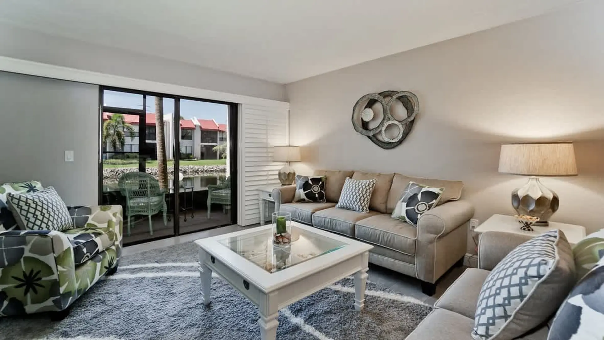 Living room with a beige sofa, patterned accent chair, coffee table, and sliding glass doors to a pa