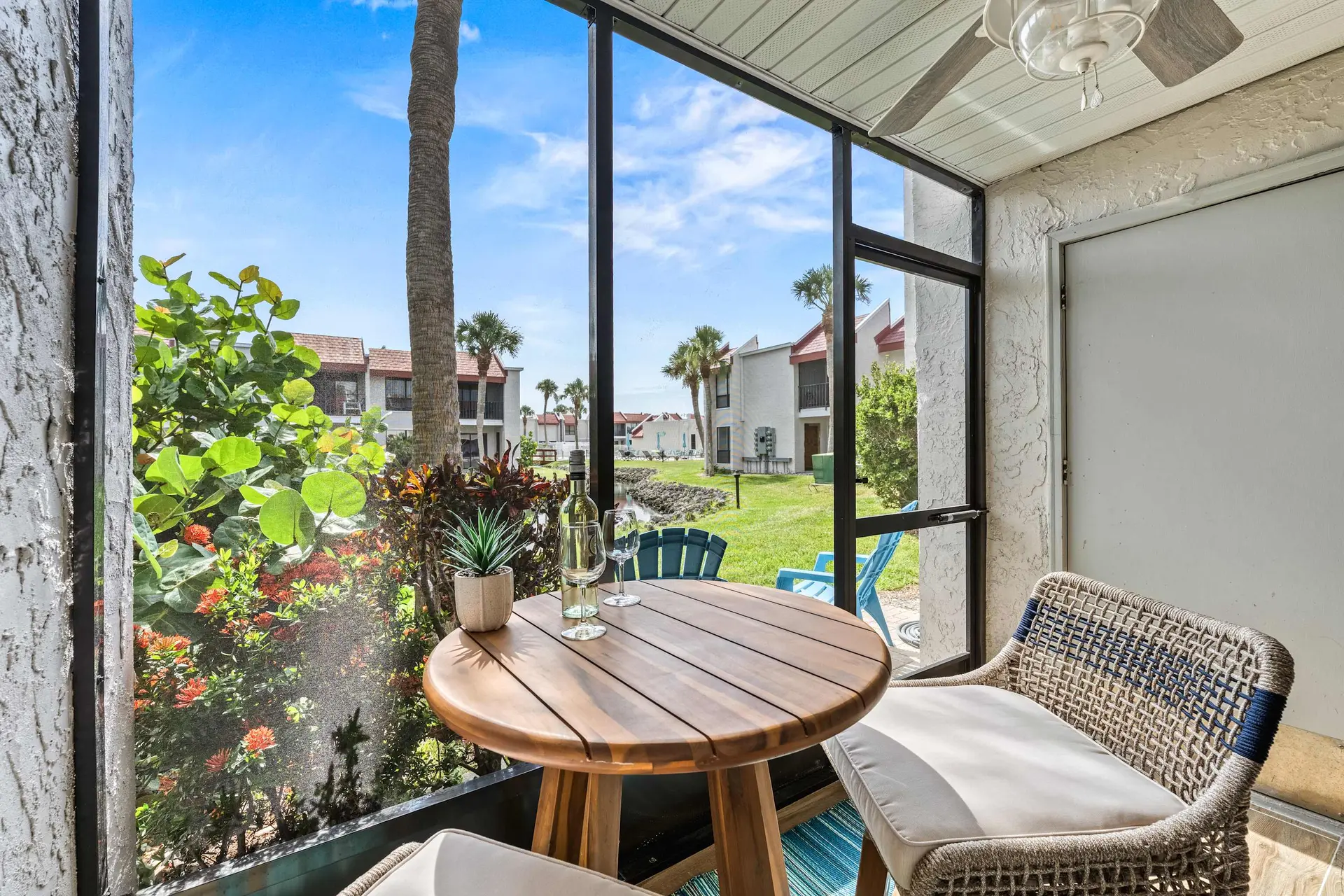 Outdoor dining area with table, chairs, and a bottle of wine on a screened-in patio.