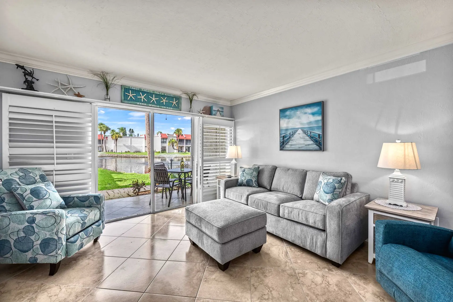 A living room with a sofa, armchair, and ottoman overlooking a patio and water.