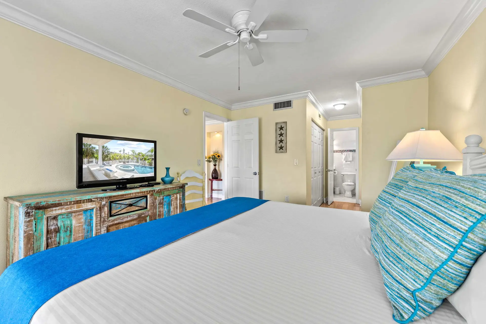 A bedroom with a tv, ornate dresser, and a bed with a blue runner.