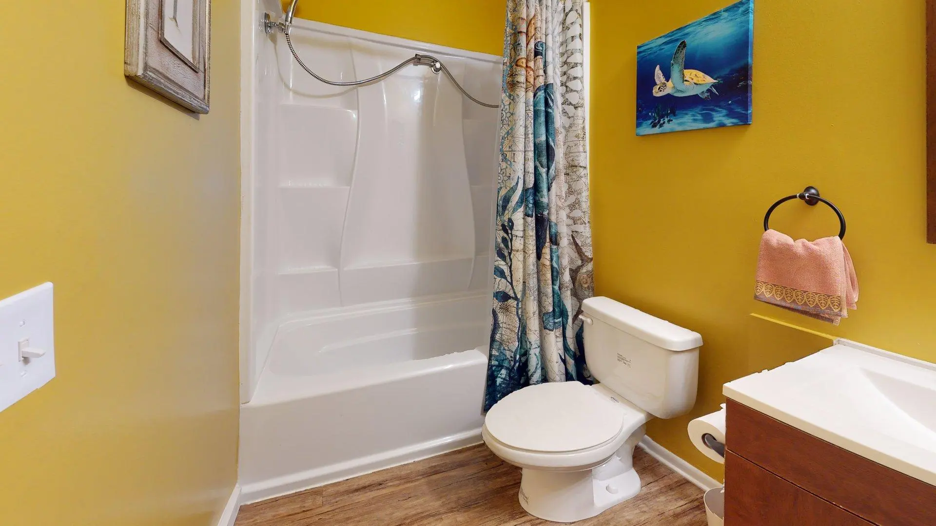 A bathroom with a yellow wall, white bathtub, and a toilet with a decorative shower curtain.