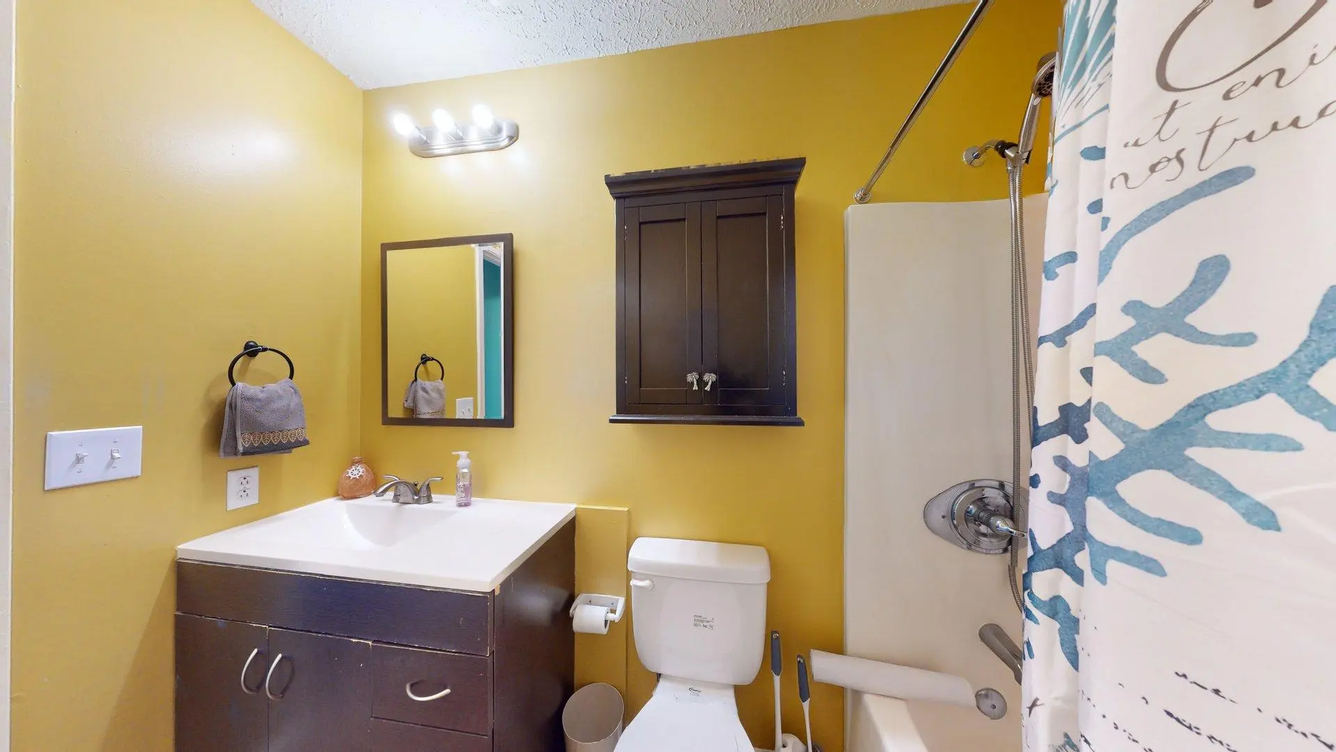 A bathroom with yellow walls, a dark wood vanity and medicine cabinet, and a blue coral shower curta