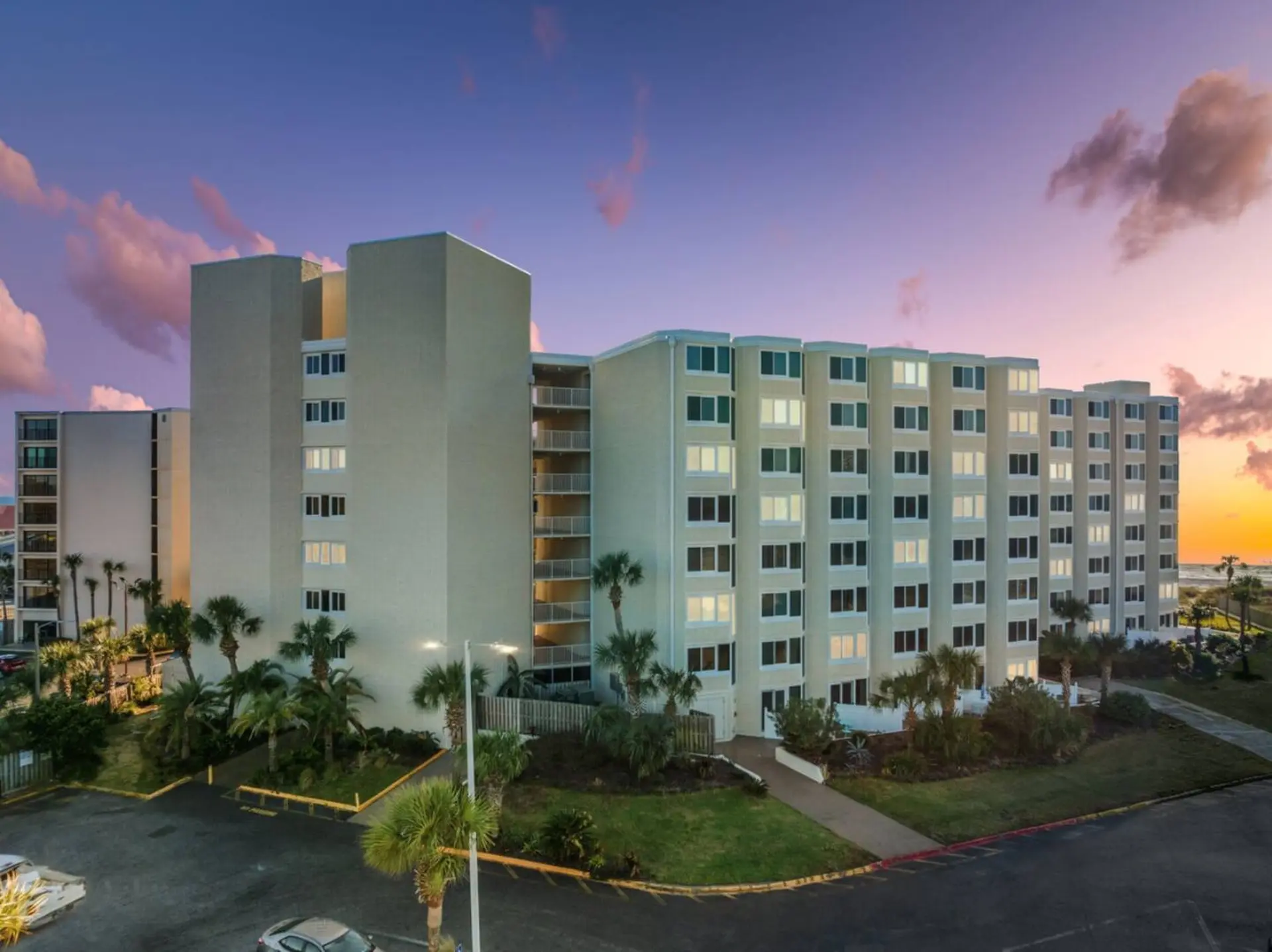 A beige apartment building stands under a purple and orange sunset sky.