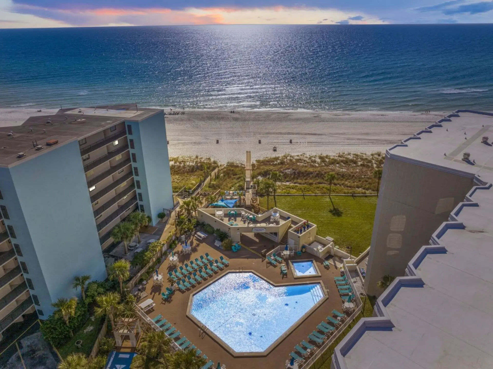 Resort pool and beach with ocean views at sunset.