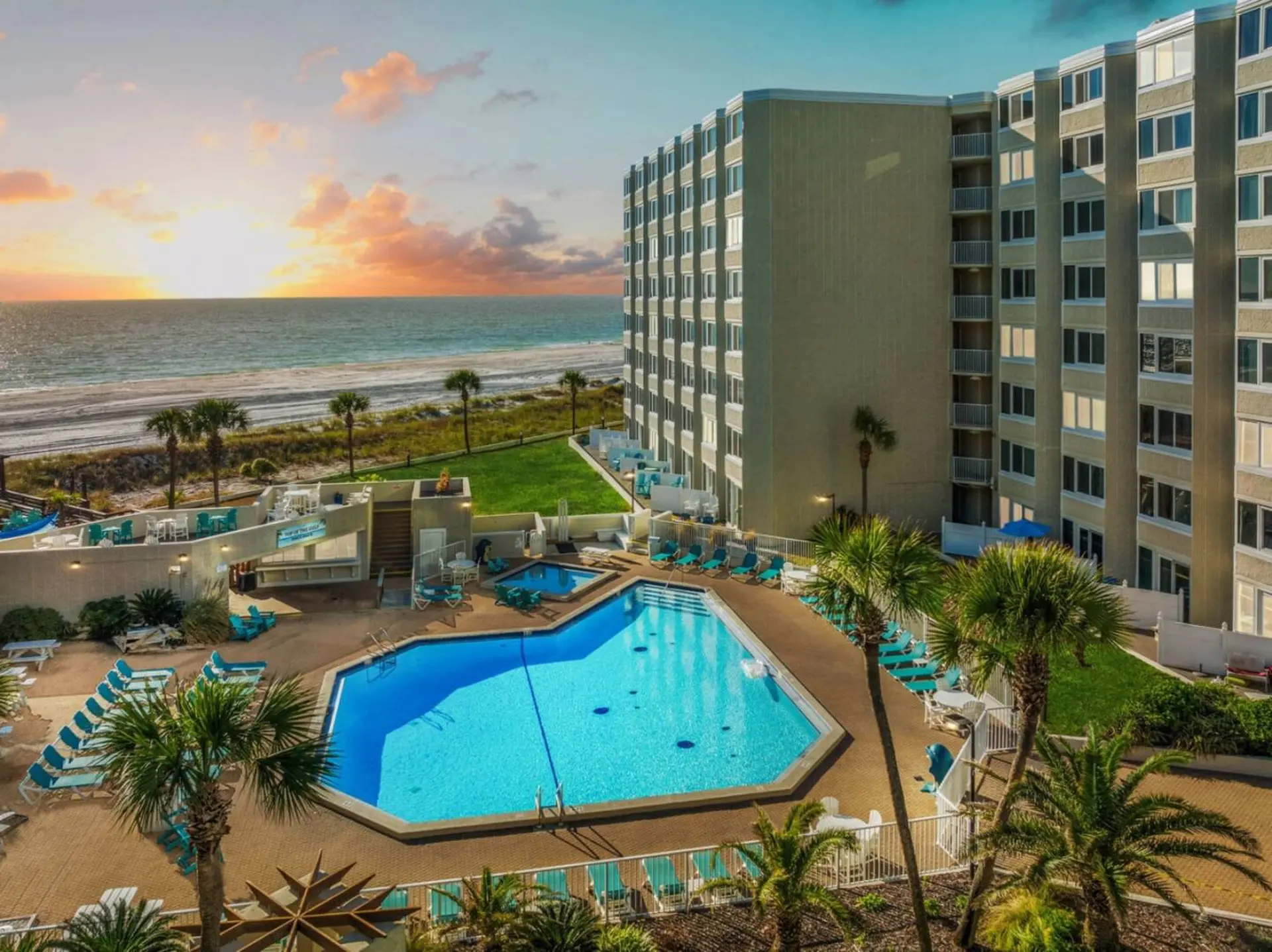 A resort pool and building sit on the beach at sunset.