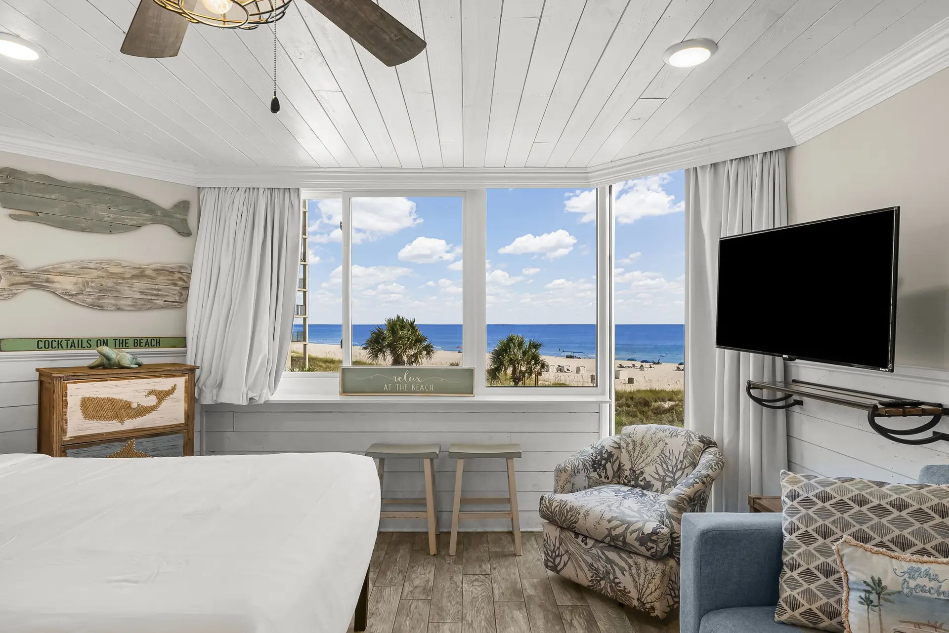 Beach view bedroom with a large window, TV, and seating area.