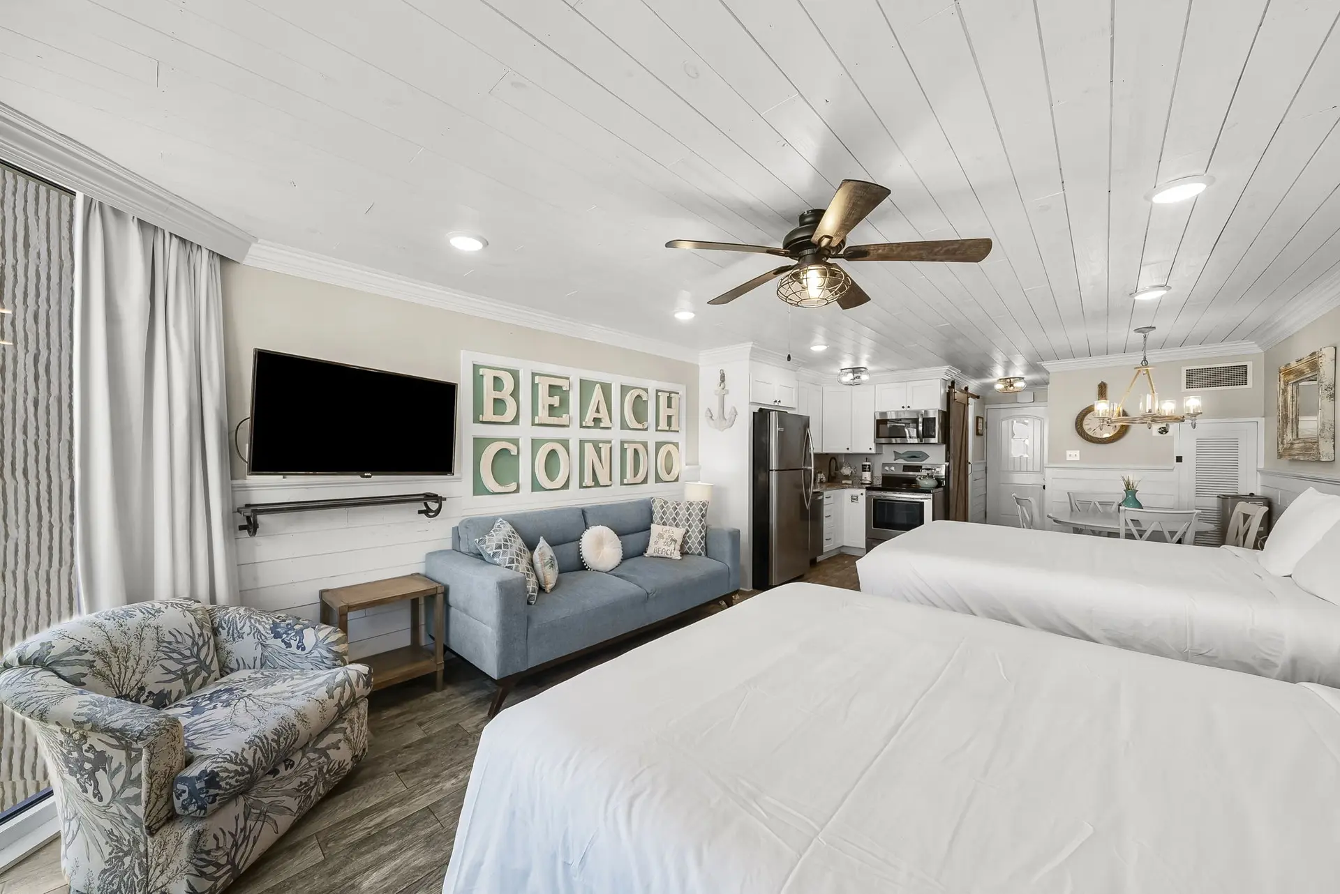 A studio apartment with two beds, a blue sofa, and a kitchen area.