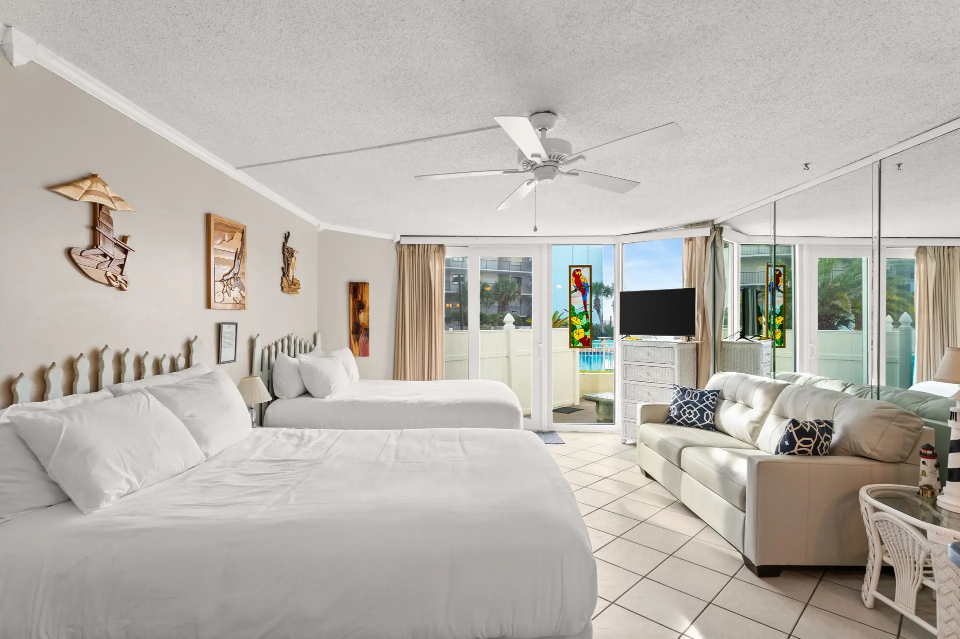 A hotel room with two beds and a couch, overlooking a pool.