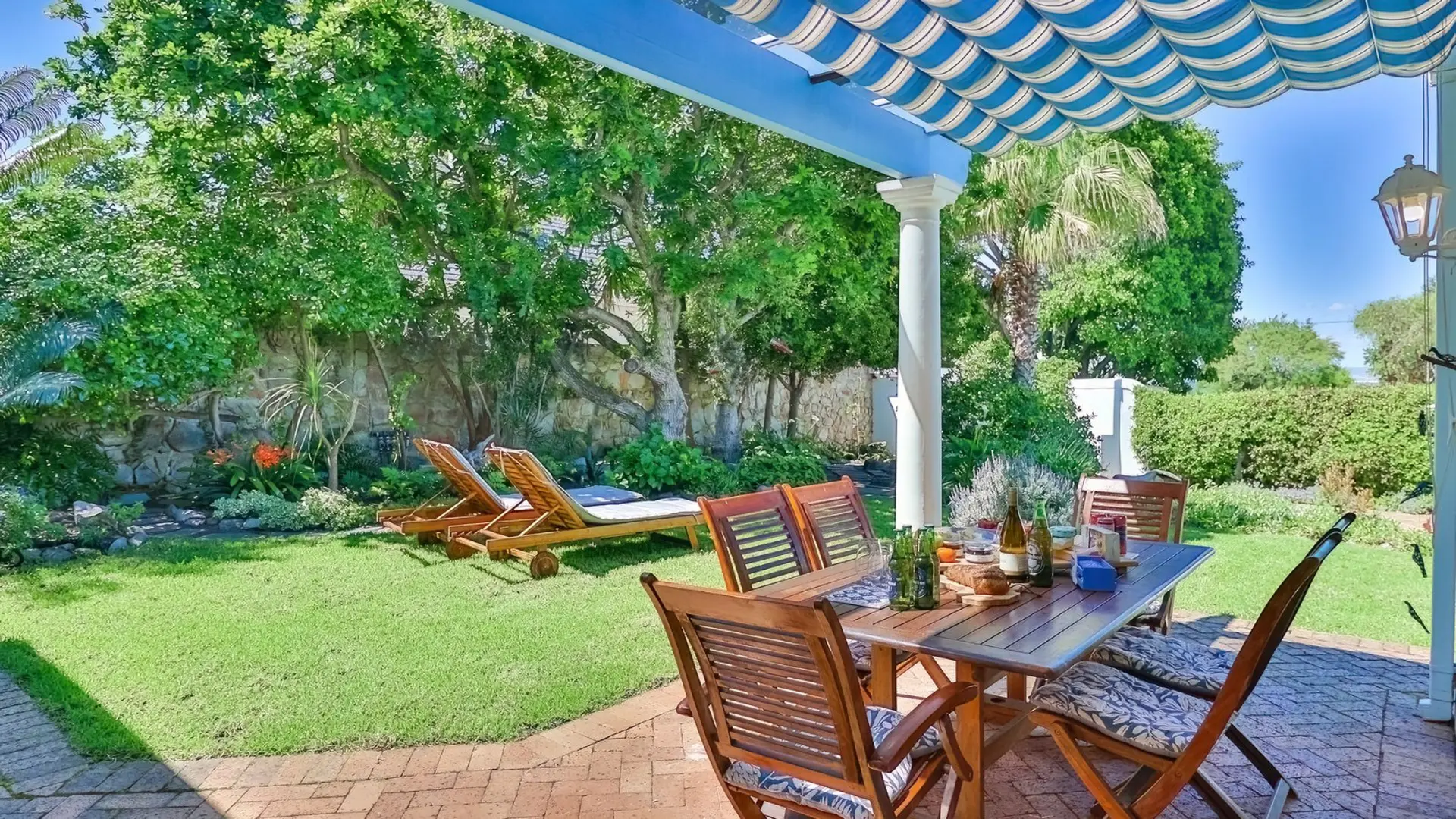 Outdoor patio with table, chairs, lounge chairs, and lush garden.