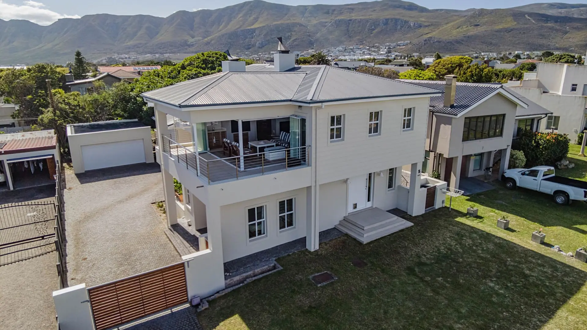 A large modern house with a metal roof and a balcony overlooking a green lawn and mountains.