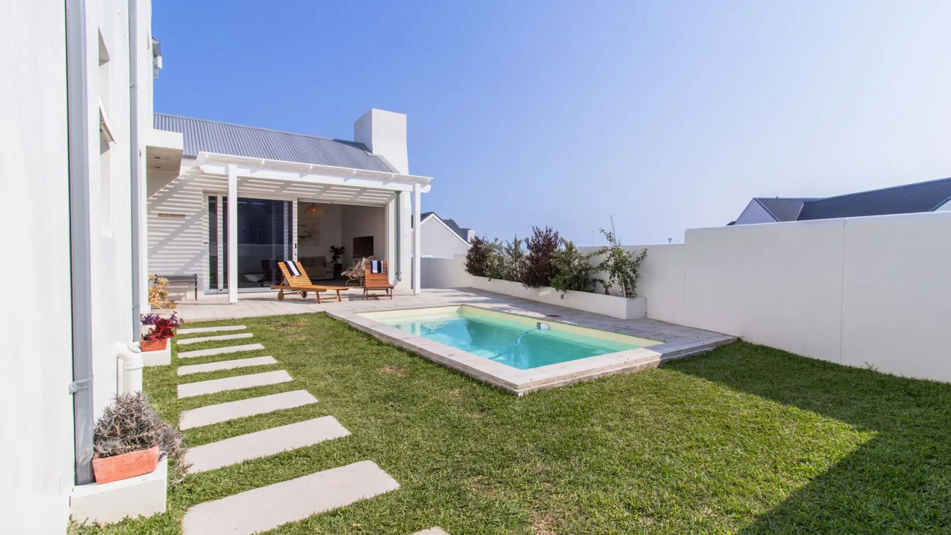 A modern home with a swimming pool, lounge chairs, and a grassy backyard.