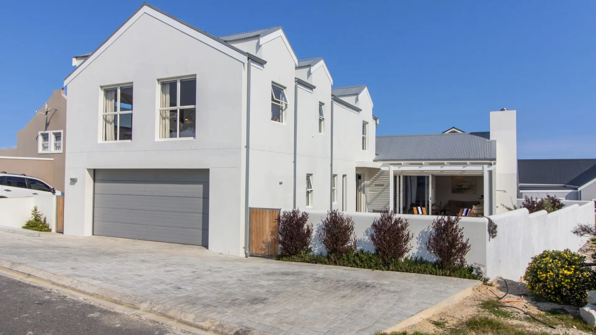 A modern white house with a gray garage door and a paved driveway under a clear blue sky.