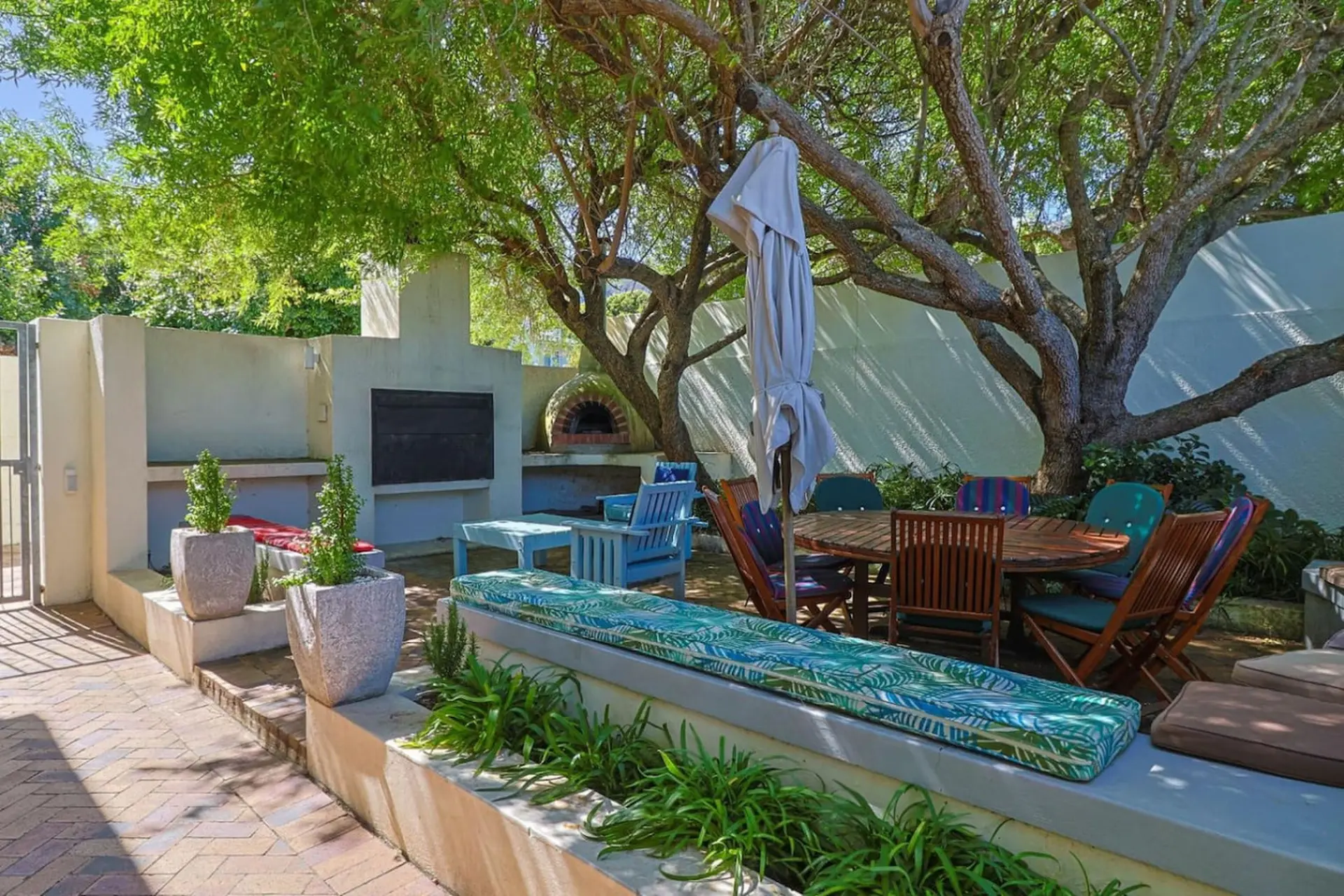 Outdoor patio with built-in grill, pizza oven, and a circular dining table under a large tree.