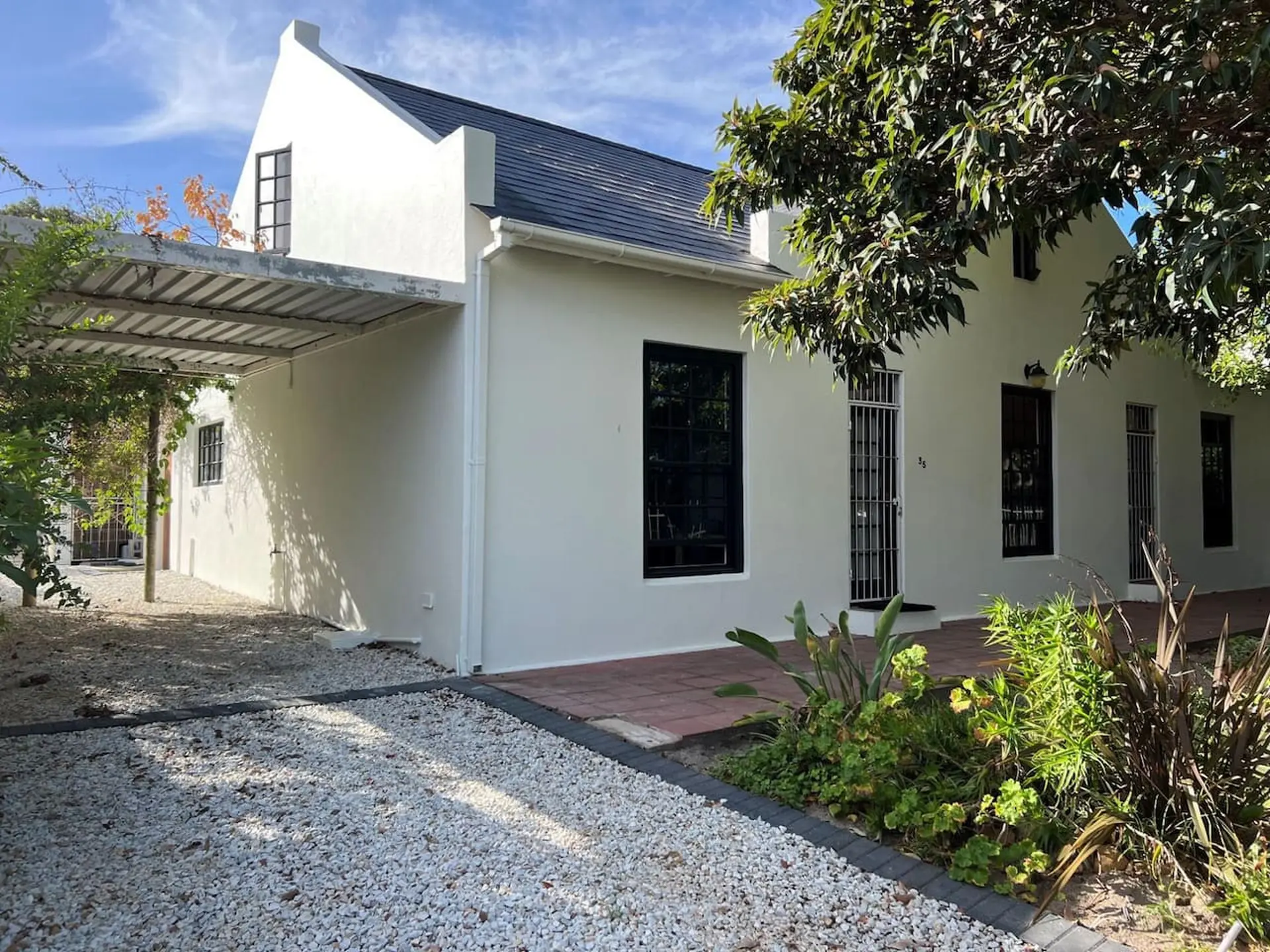 A white house with a dark roof and gravel driveway on a sunny day.