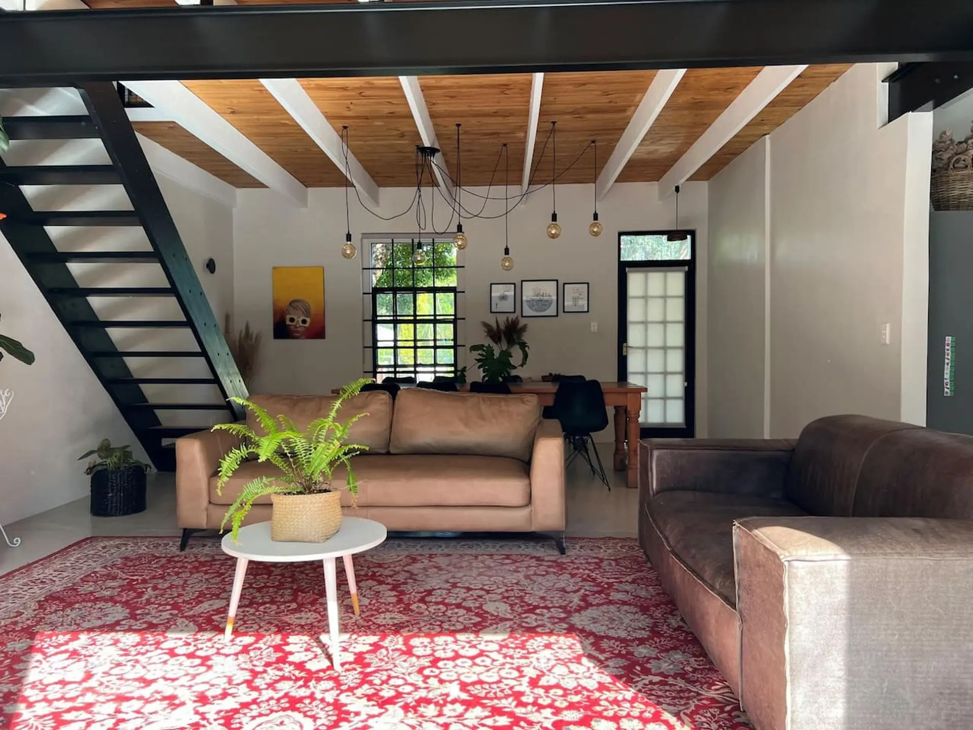 Modern living room with a brown leather sofa and a tan couch, a red patterned rug, and a staircase.