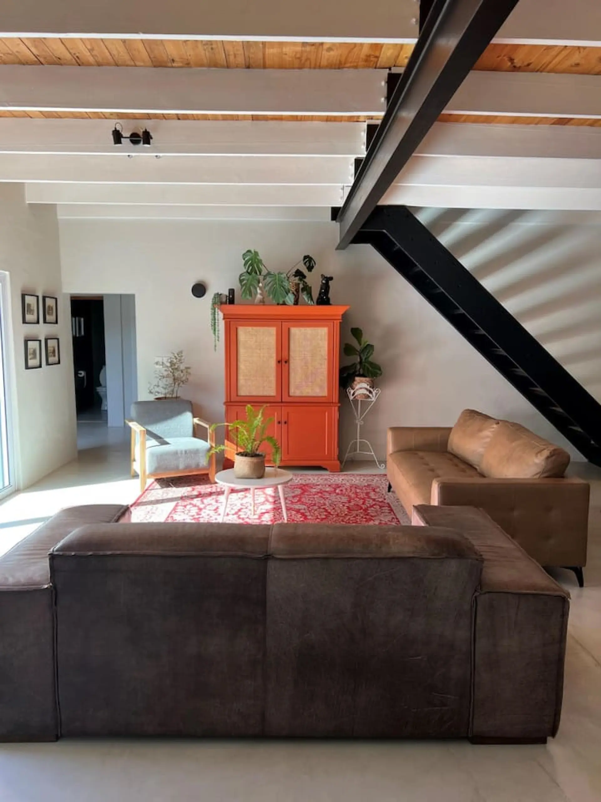 A living room with exposed beams, a steel staircase, and brown leather sofas.