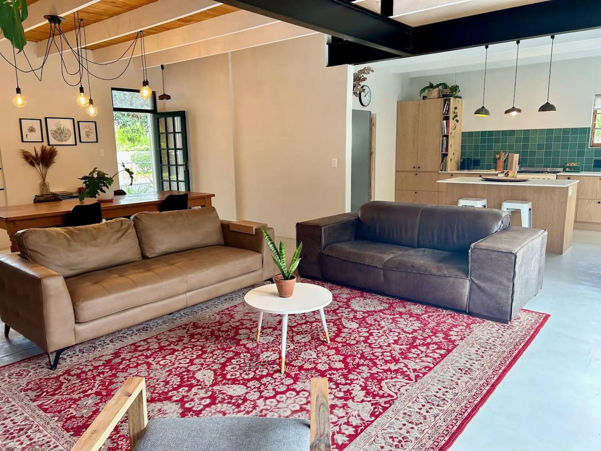Two leather couches on a red Persian rug in a living room with a kitchen and dining table in the bac
