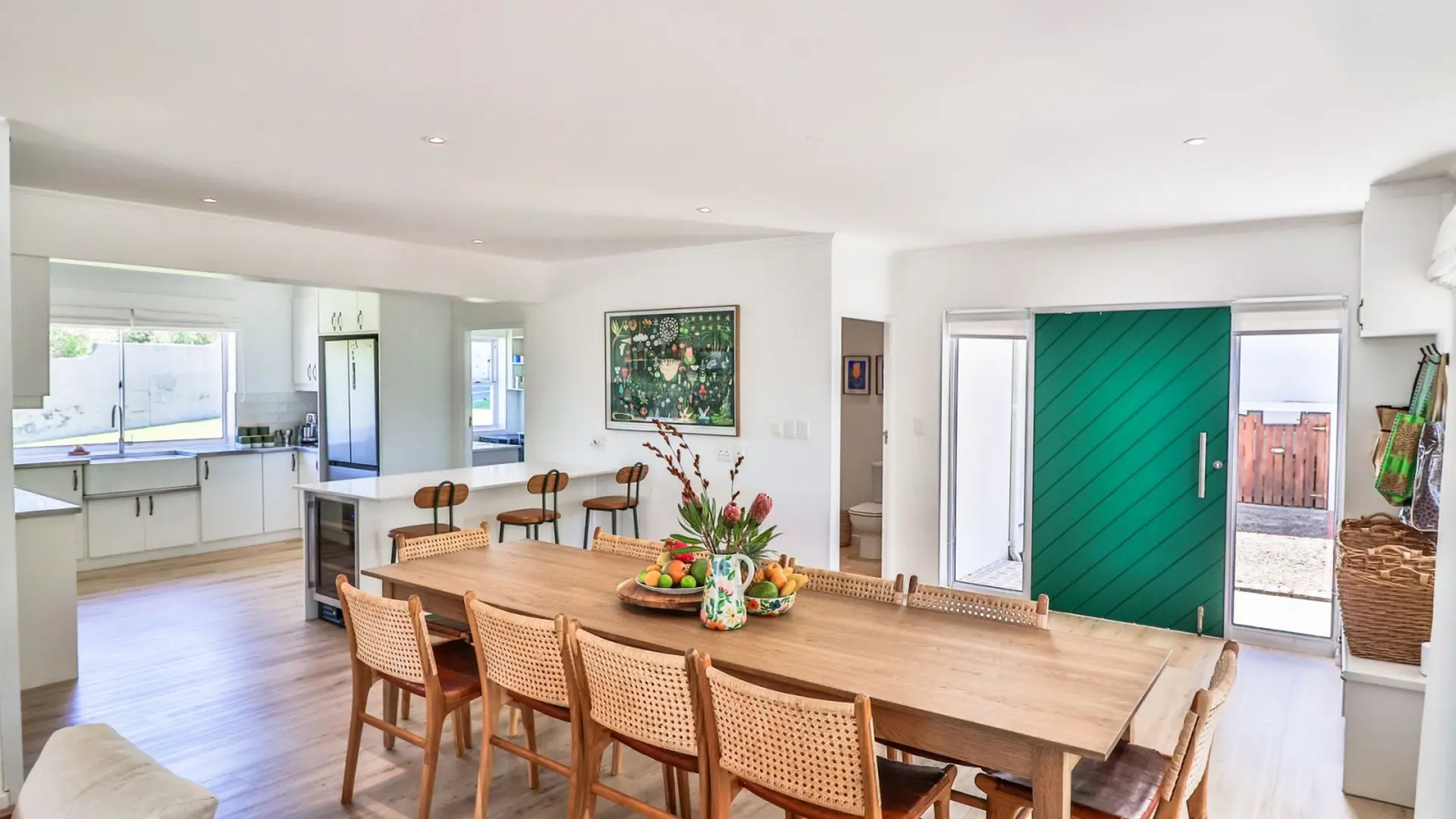 Modern dining room with a large wooden table and chairs, a green sliding door, and a kitchen.