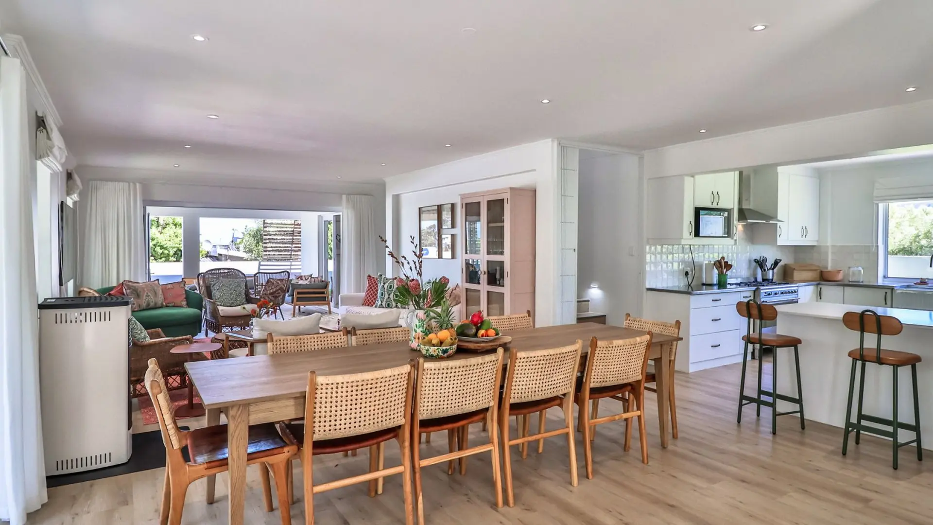 A bright dining area with a wooden table and chairs, adjacent to a modern kitchen with a breakfast b
