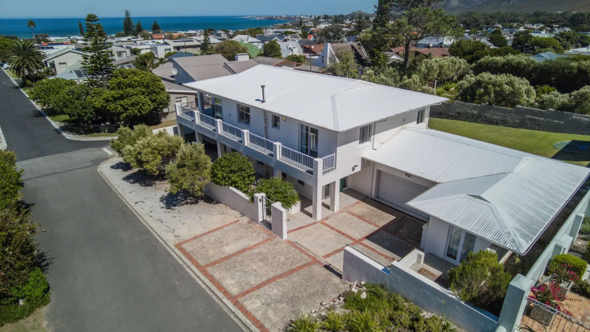 Aerial view of a modern white house with a corrugated roof, surrounded by greenery and overlooking a