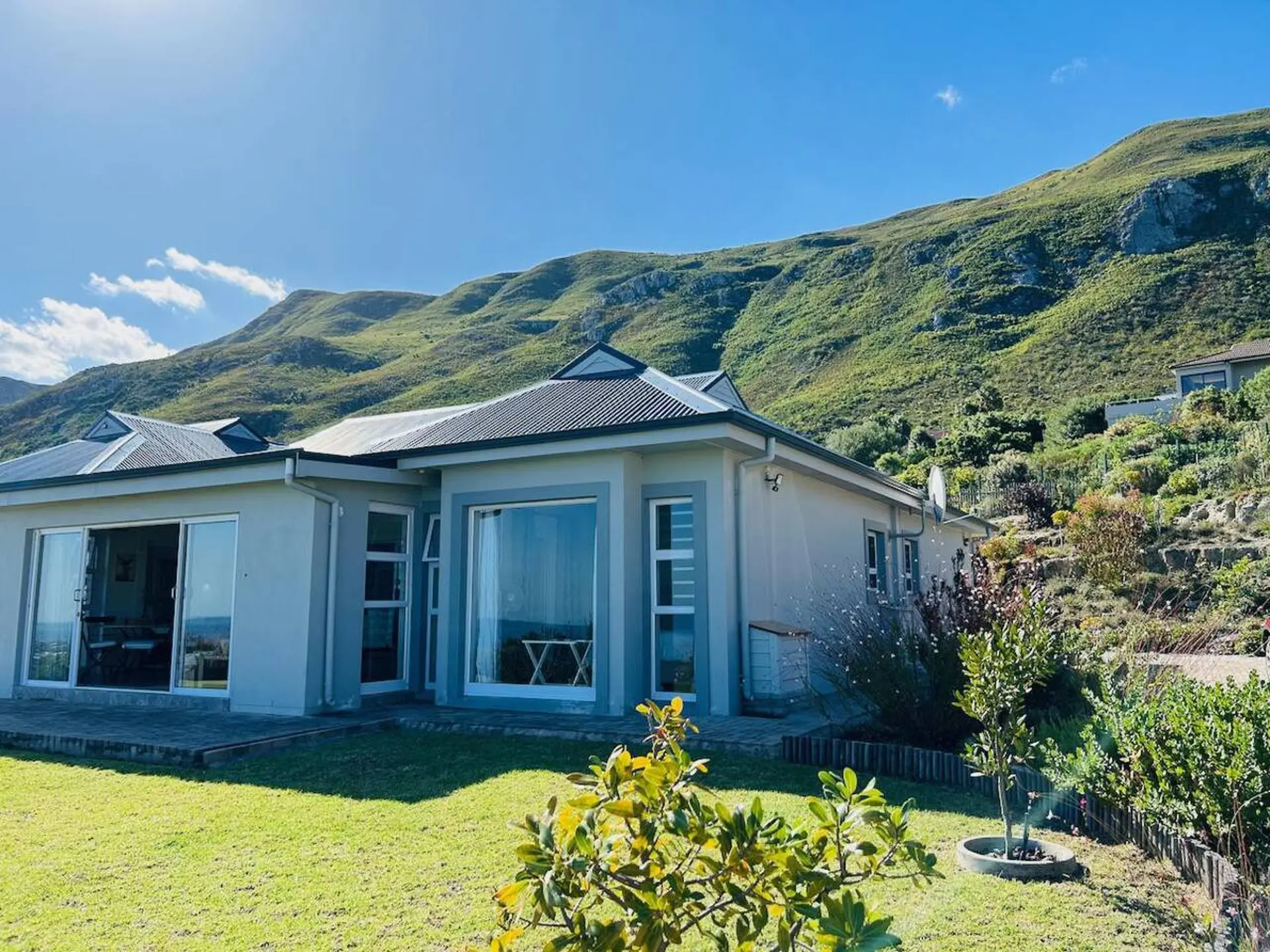A modern house with large windows sits at the base of a lush green mountain.