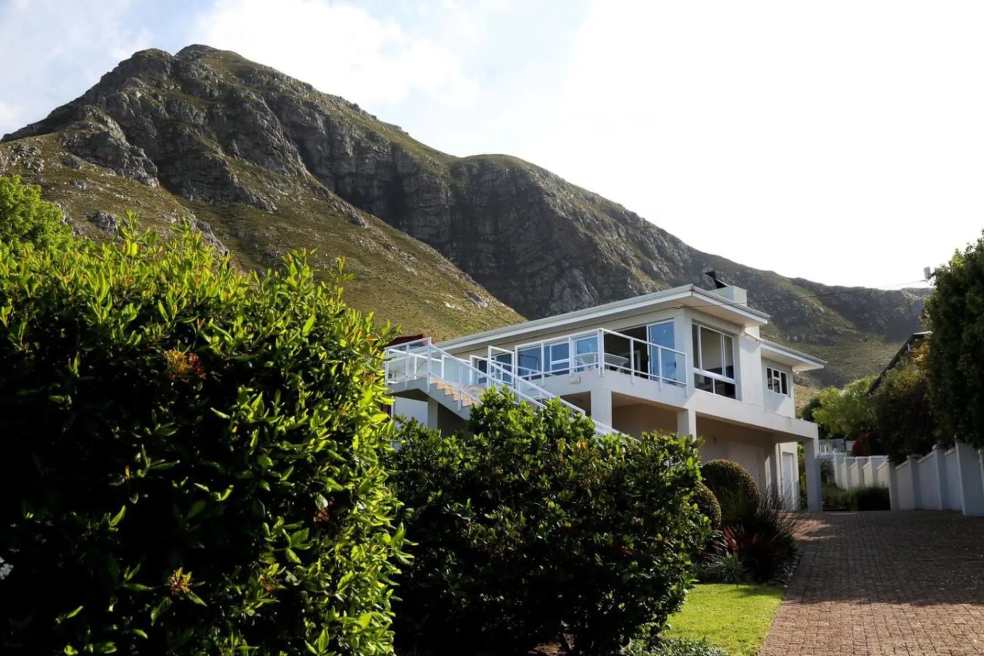 A modern house with a glass balcony sits against a backdrop of a rugged mountain.