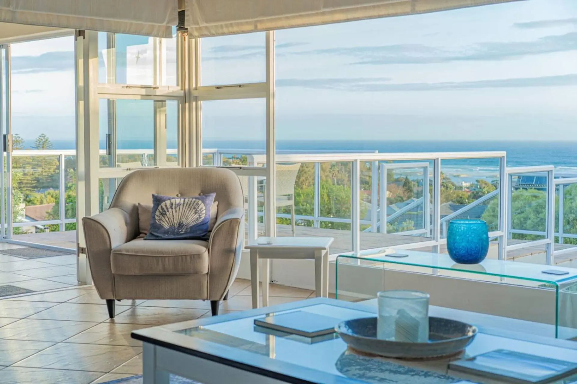 Living room with ocean view and armchair with seashell pillow.
