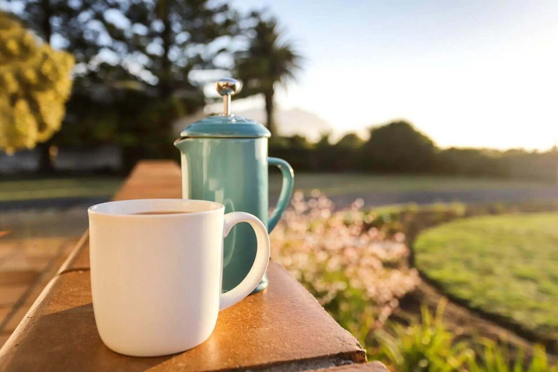 A white mug of coffee sits on a ledge next to a turquoise French press.
