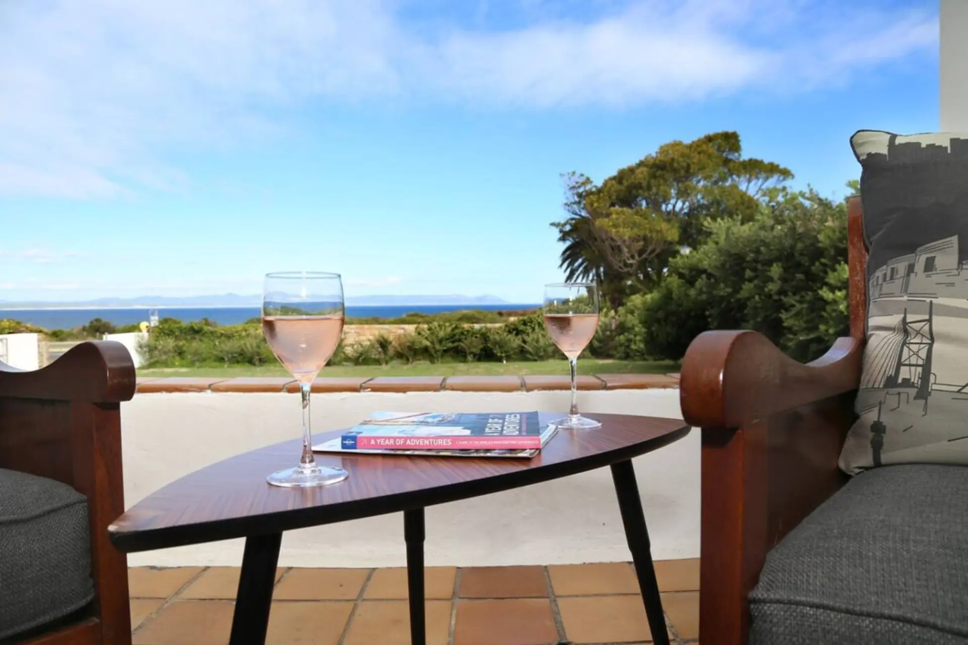 Two glasses of rosé wine on a small table with a book, overlooking the ocean.