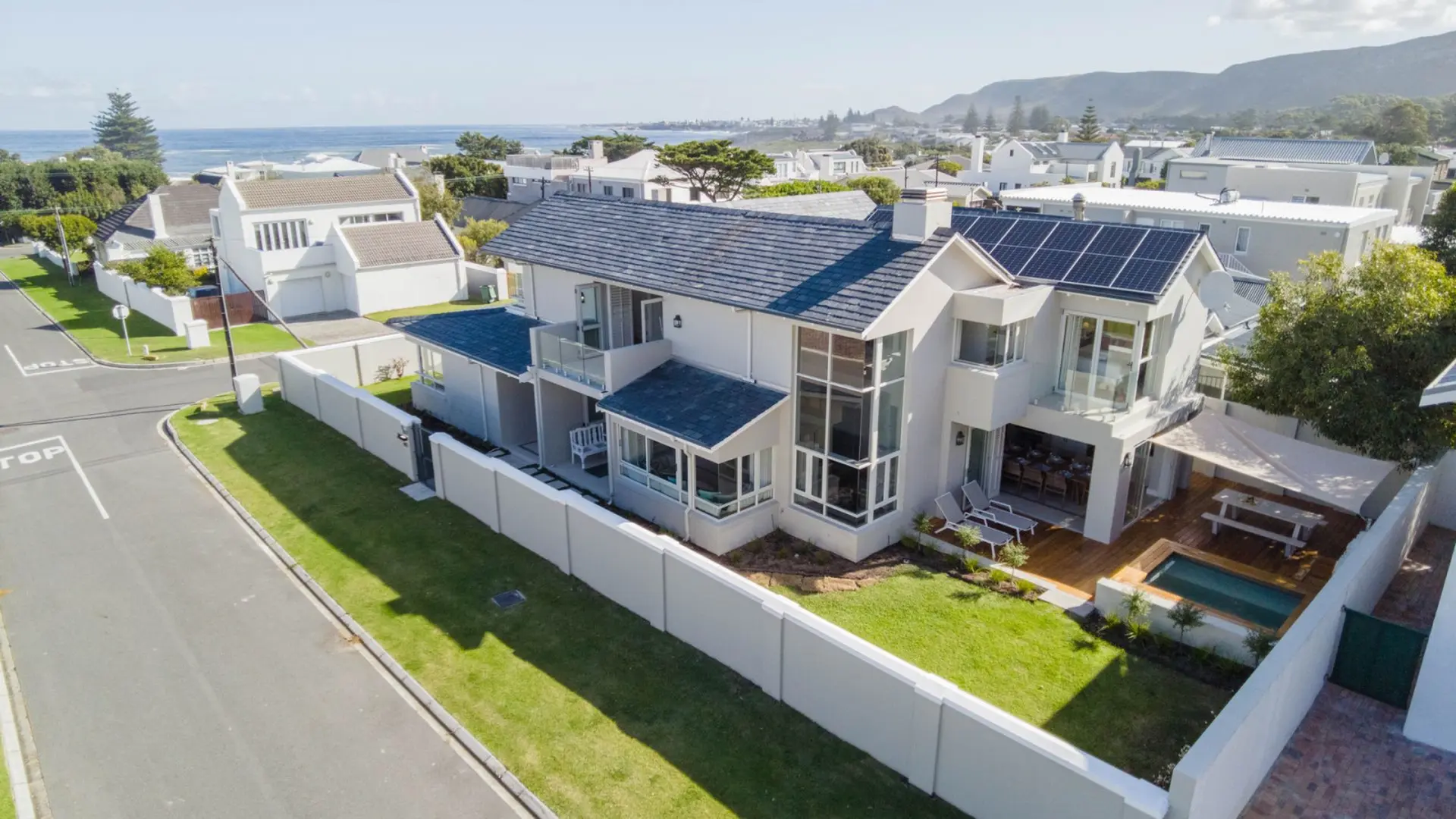A modern house with a pool, patio, and solar panels in a coastal town.