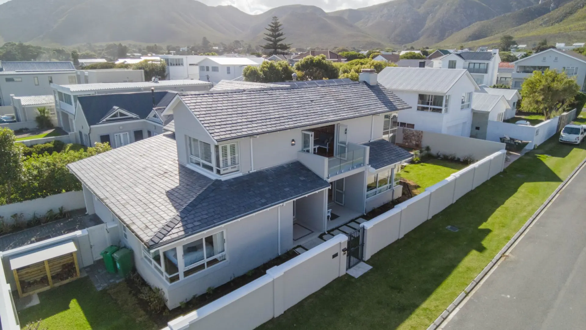 Aerial view of a modern light gray house with a dark gray roof, surrounded by a white fence and mani