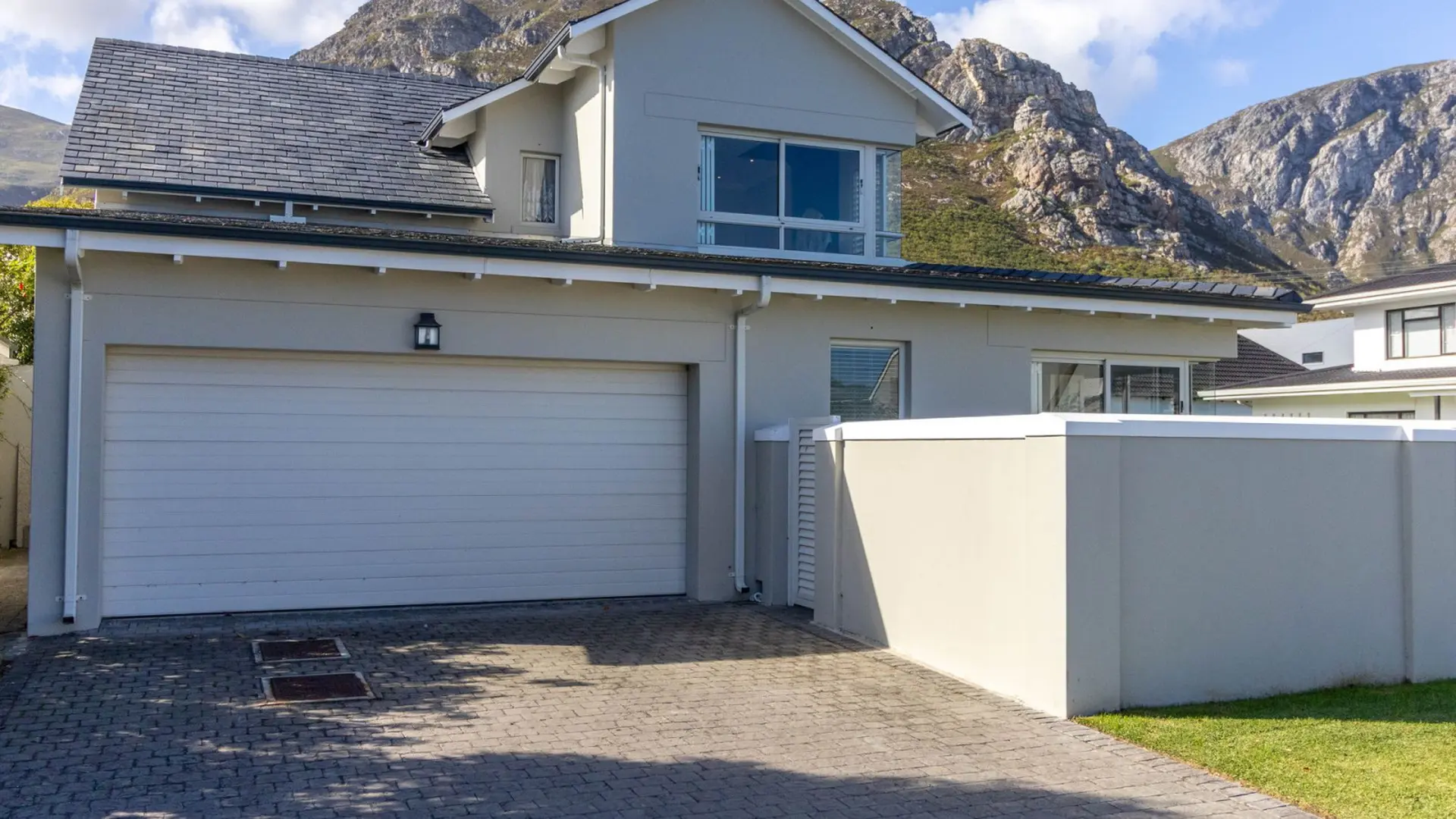 A modern grey house with a garage and driveway in front of a mountain.