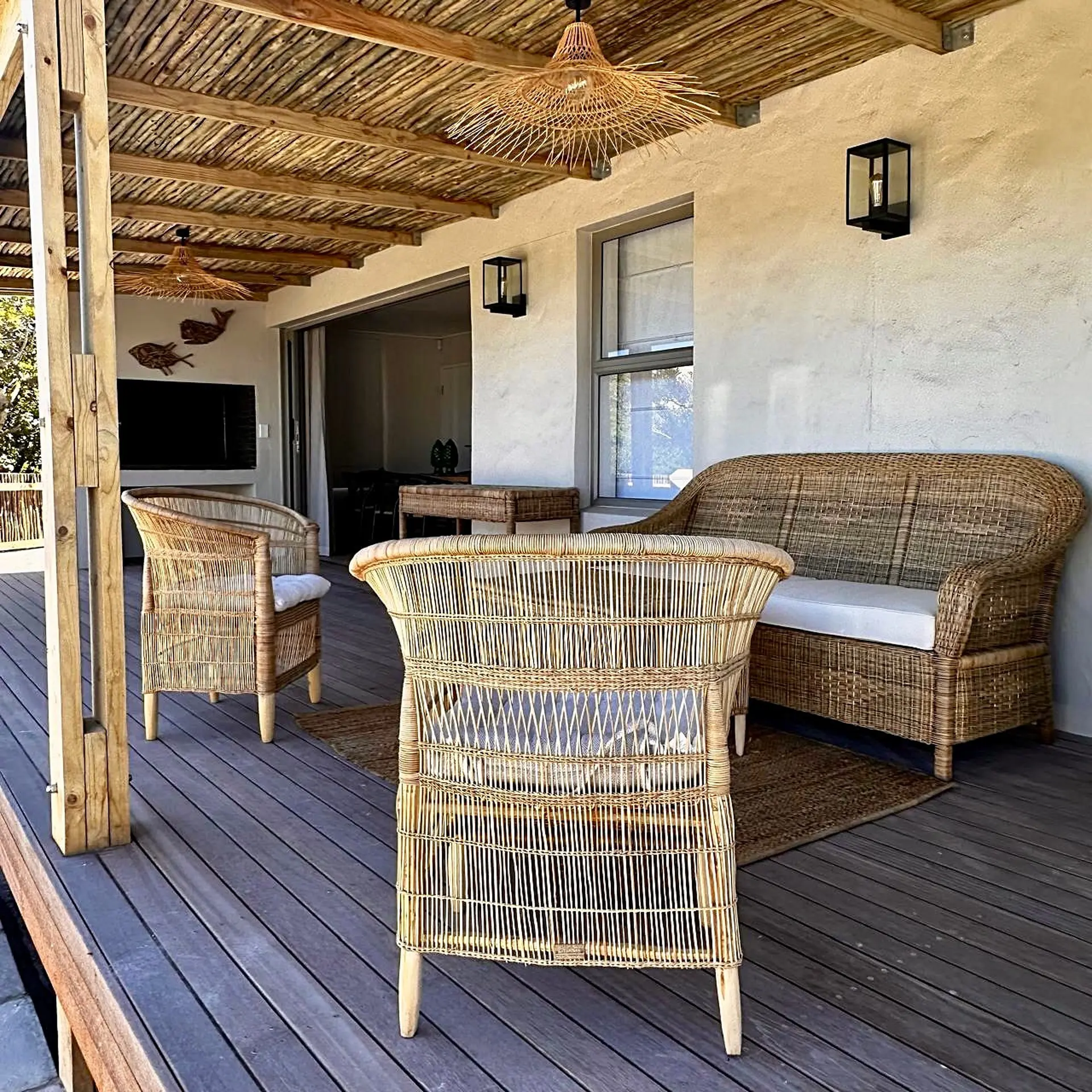 Wicker furniture on a wooden deck under a thatched roof with bamboo accents.