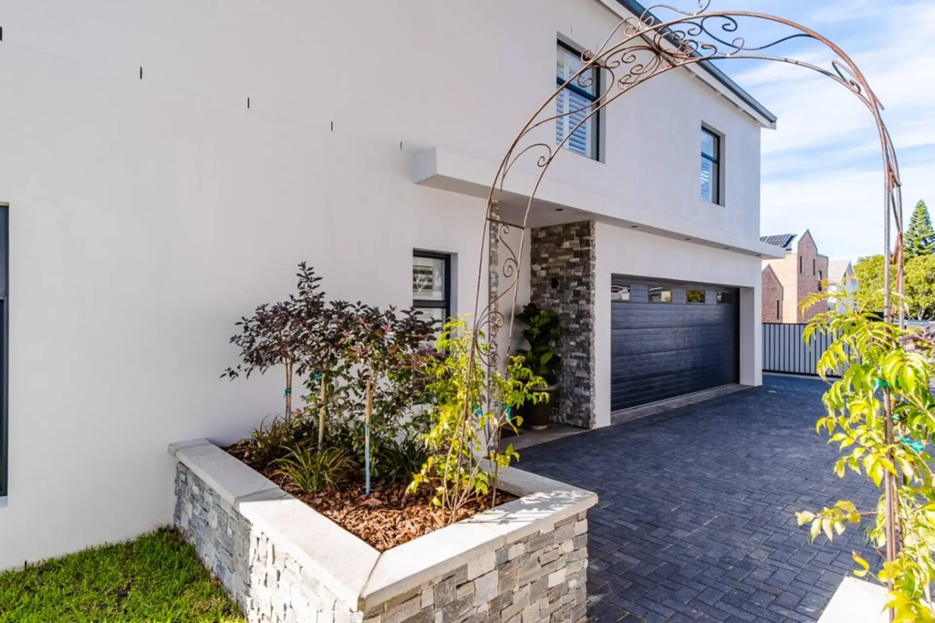 Modern home with an arched walkway, a stone-clad garage, and a lush garden.
