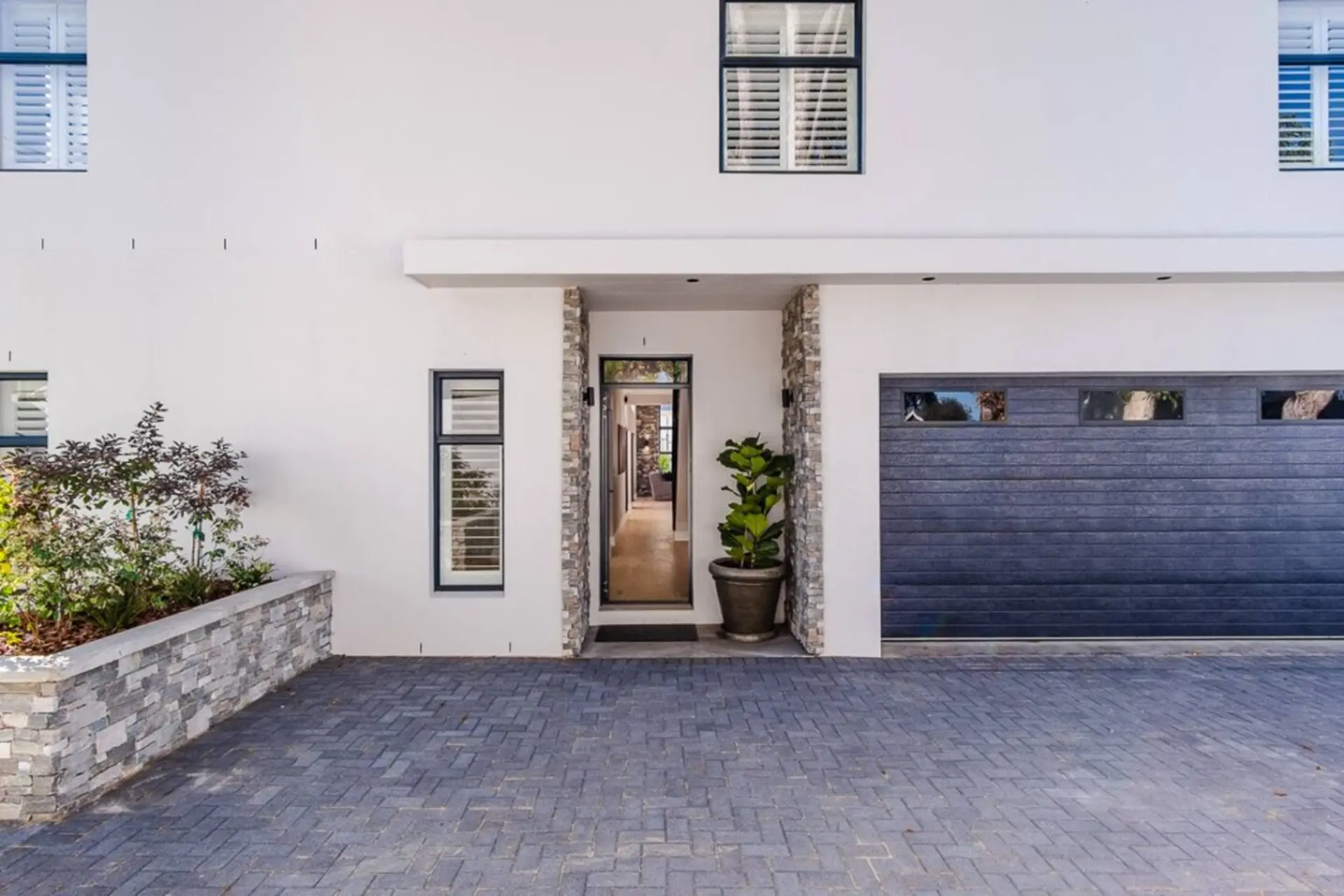 Modern white house with a dark garage door, a welcoming entryway, and a paved driveway.