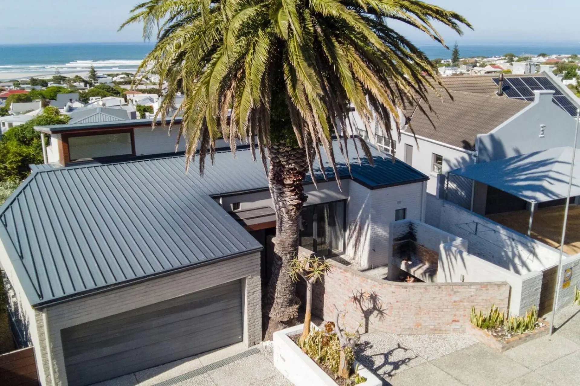 Modern home with a large palm tree in the yard and a view of the ocean.