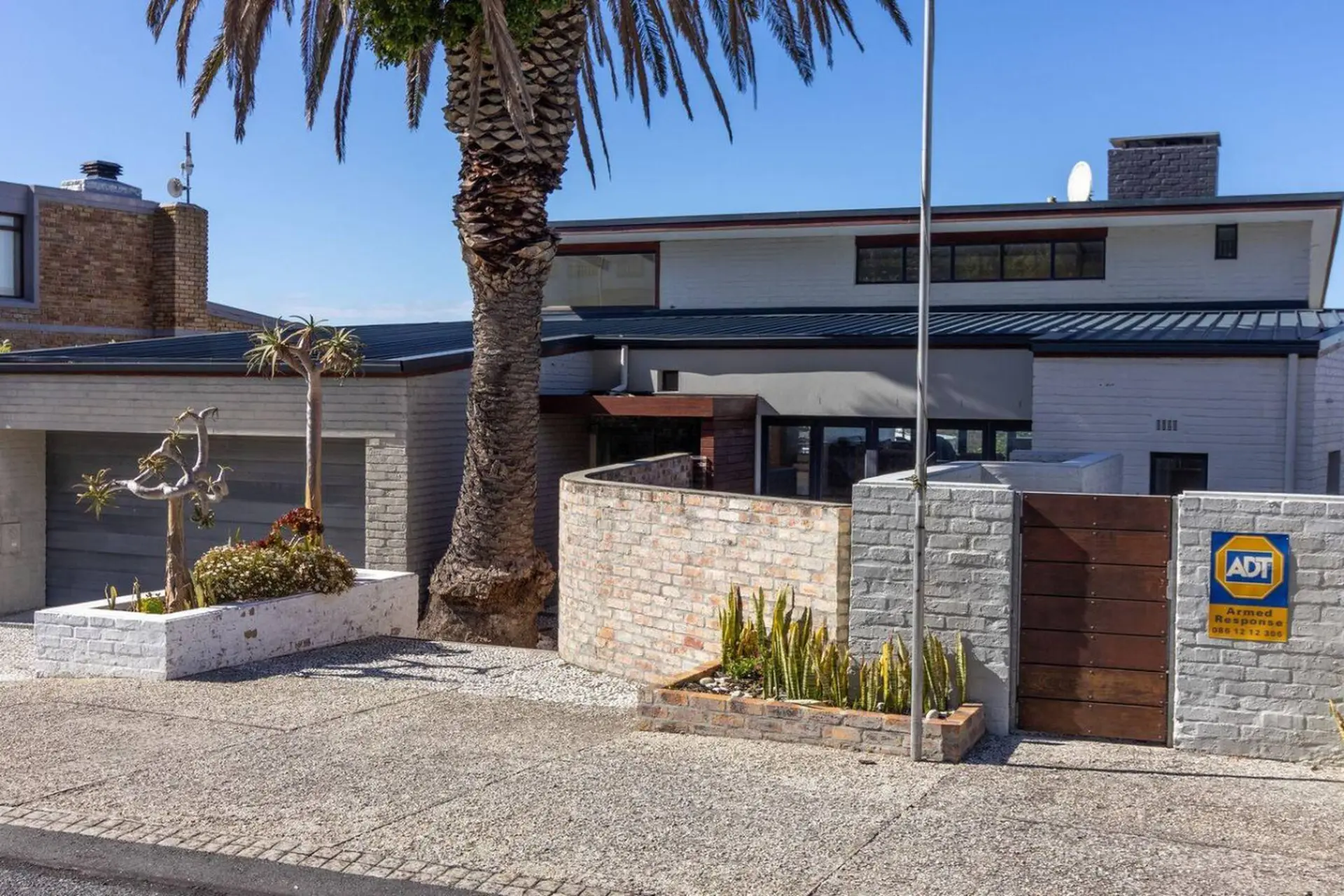 A modern house with a palm tree in front and an ADT security sign.