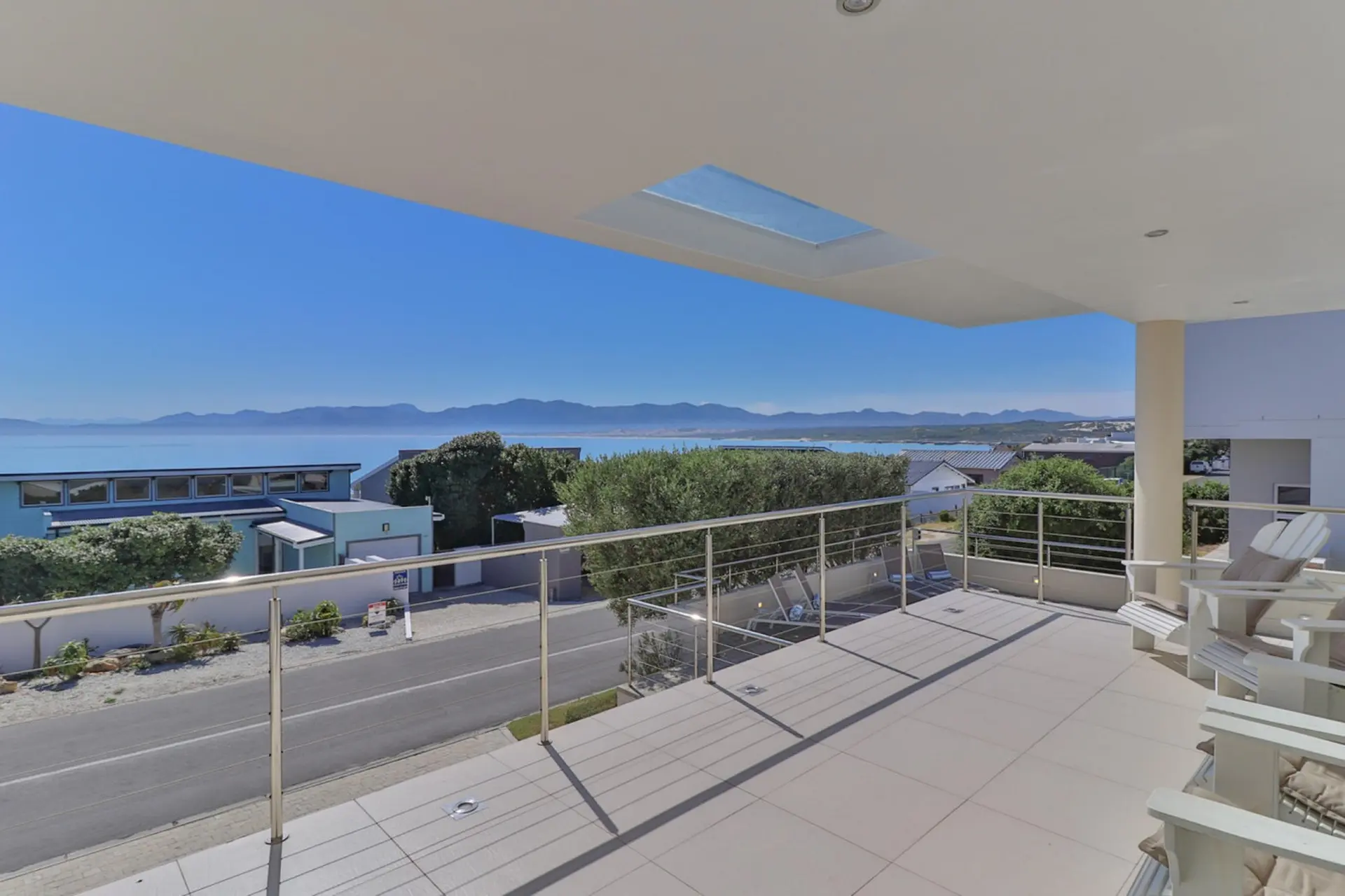 Balcony view of a bright blue sky, ocean, and distant mountains.