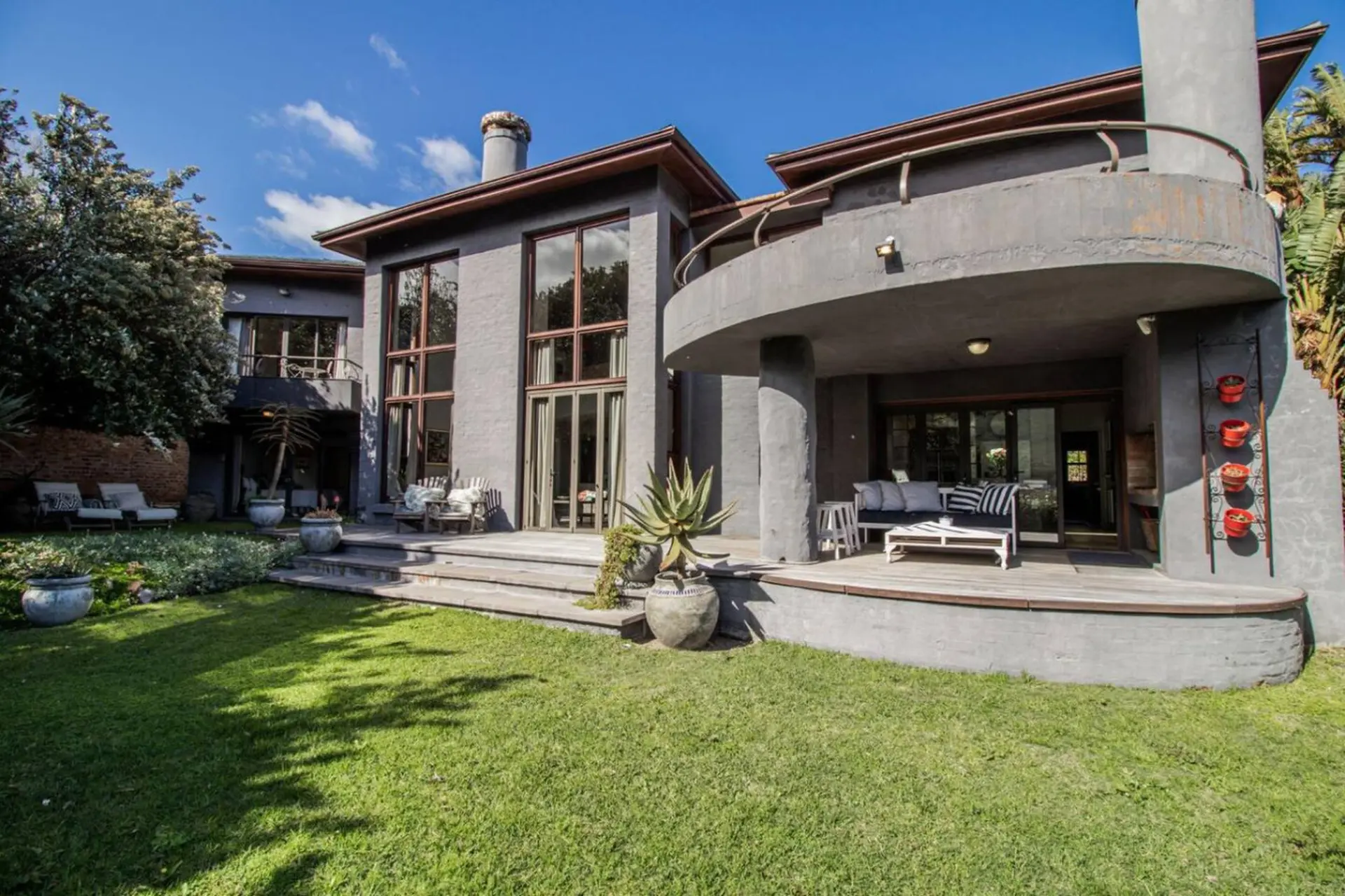 Modern gray house with large windows, a curved balcony, and a green lawn.