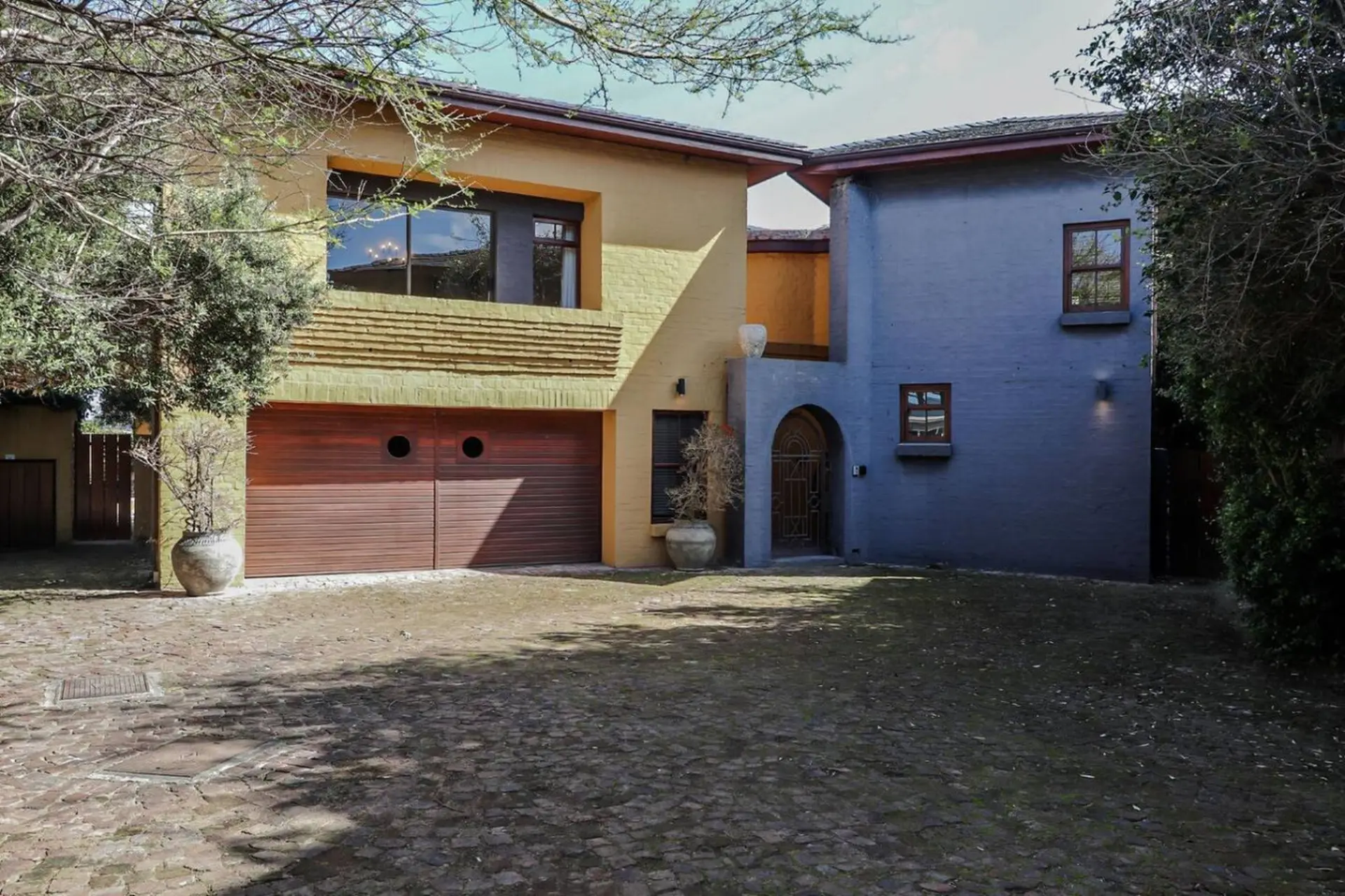A two-story house with a yellow and blue facade, a wooden garage door, and a gated entryway.