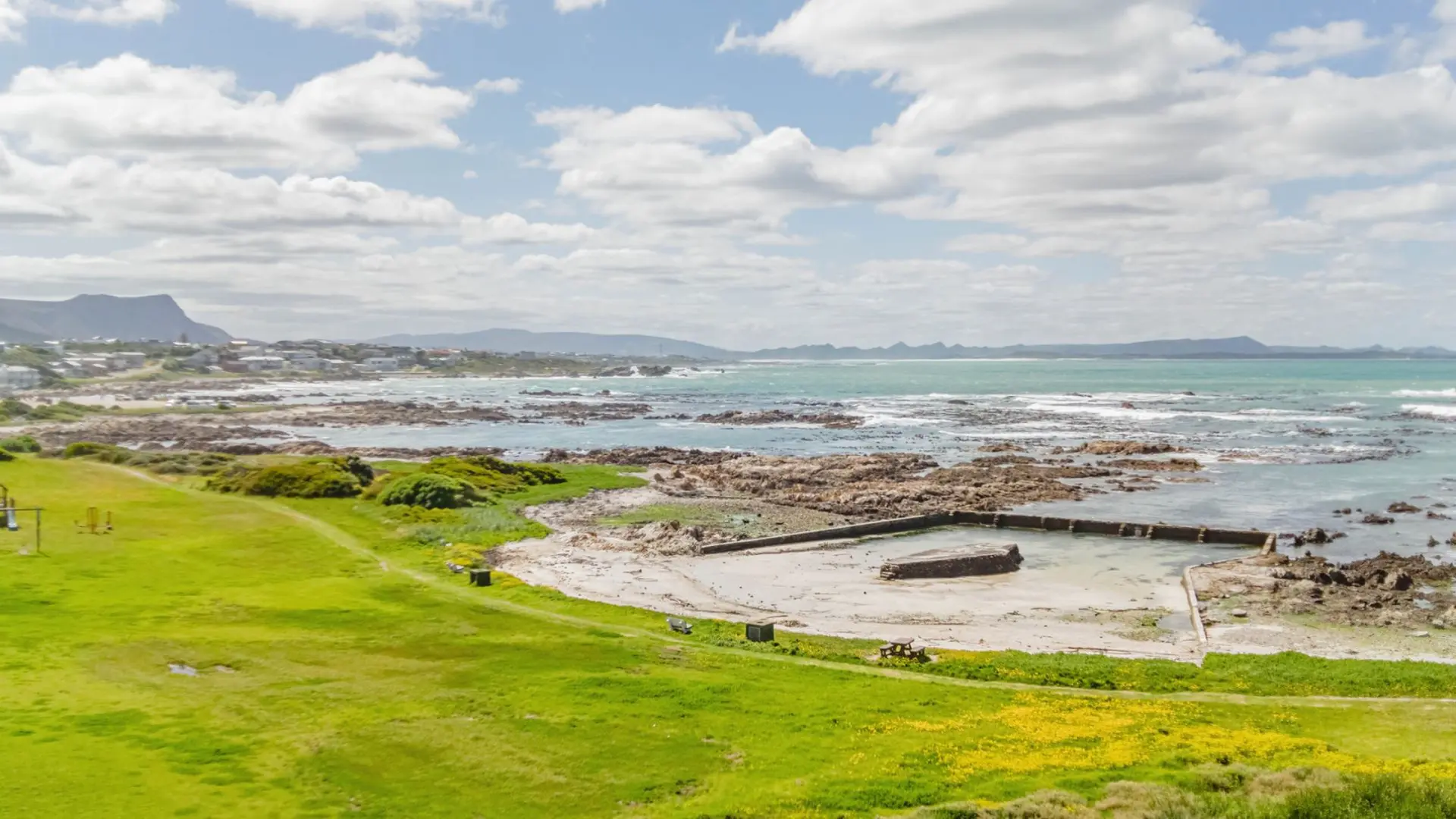 Ocean views with grassy hills, a rocky shoreline, and a man-made pool.