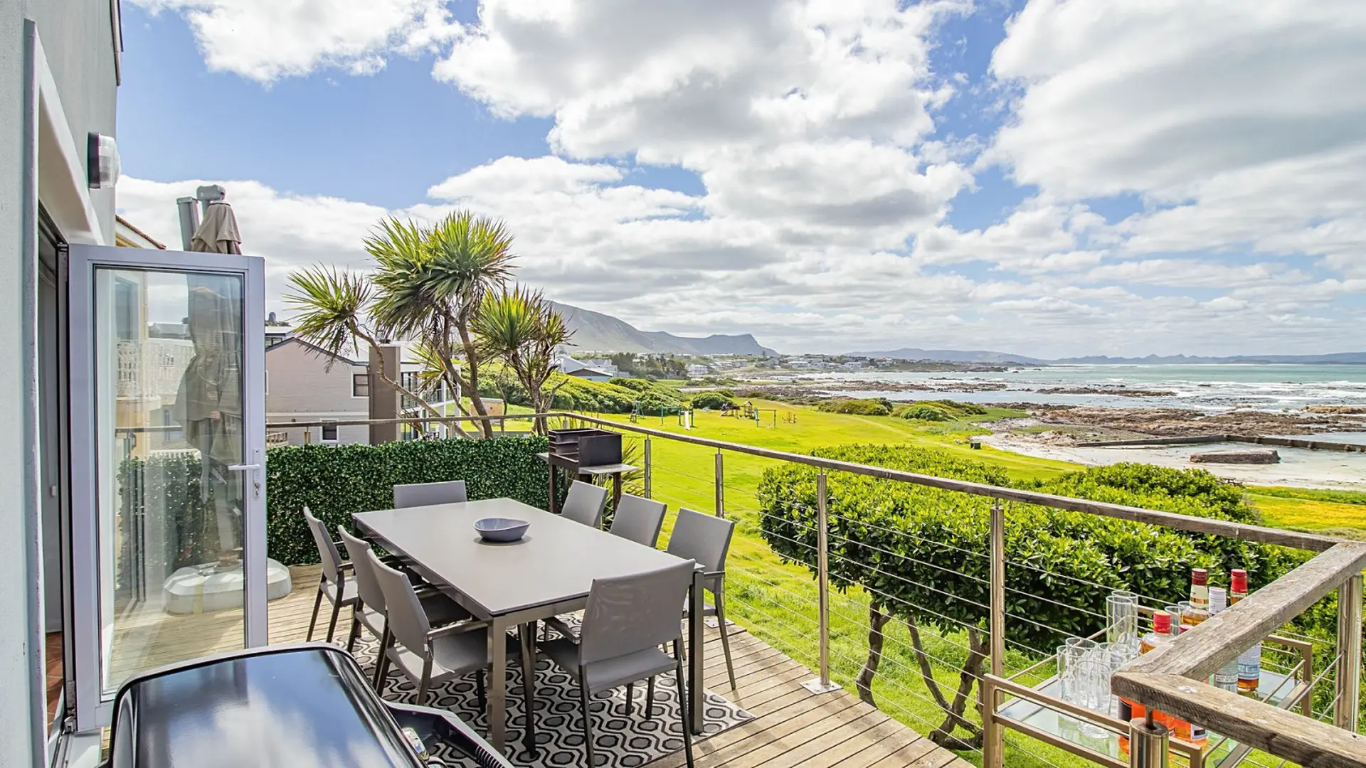 Modern deck with dining table, grill, and ocean view.